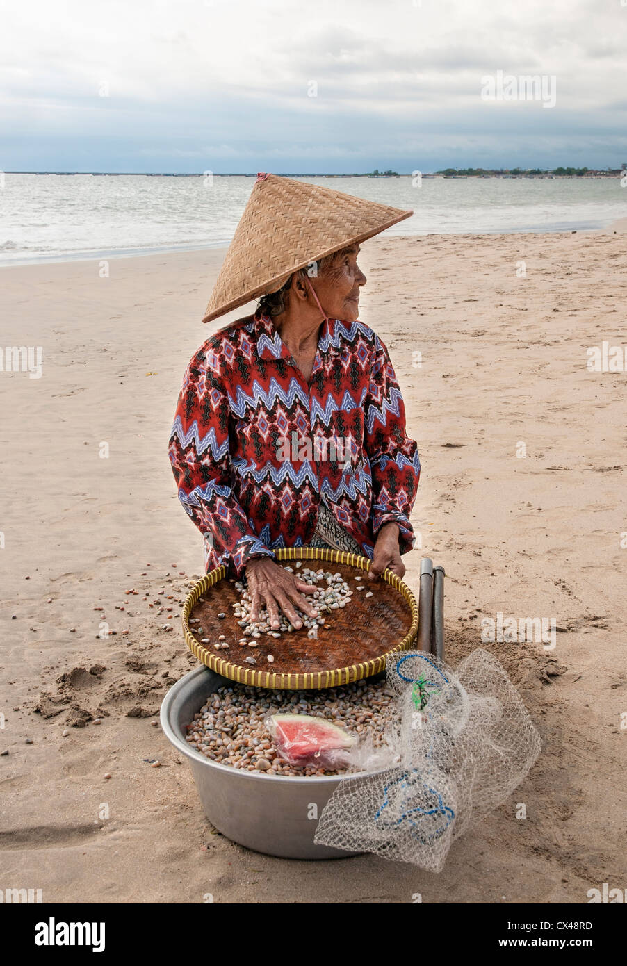 Femme la collecte des coquillages pour faire des colliers. Sur la plage de Jimbaran, péninsule de Bukit, au sud de Bali, Indonésie. Banque D'Images