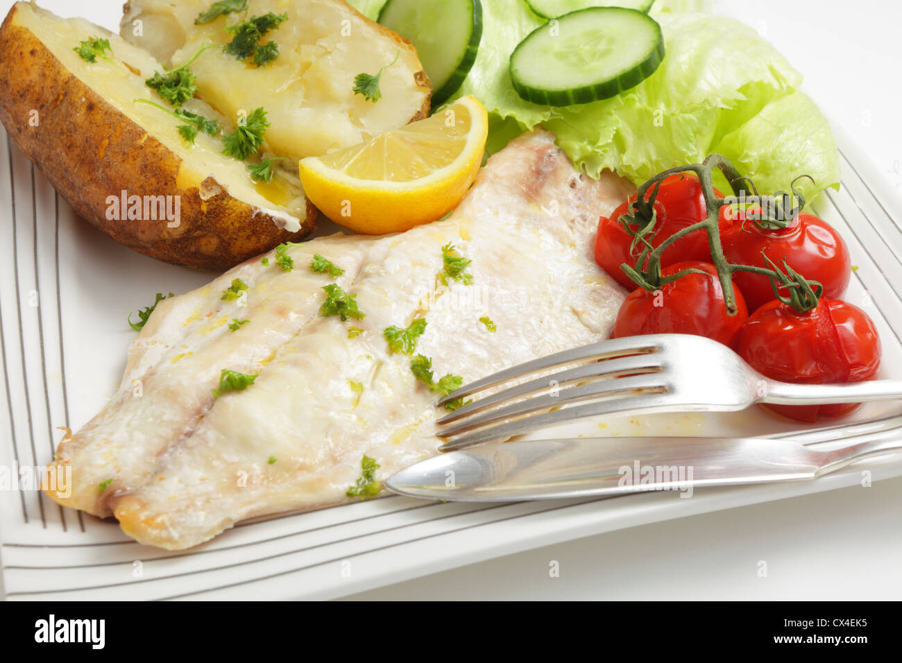 Gros plan sur un filet de poisson blanc cuit au four servi avec une pomme de terre et les tomates, une pointe de citron et une salade Banque D'Images