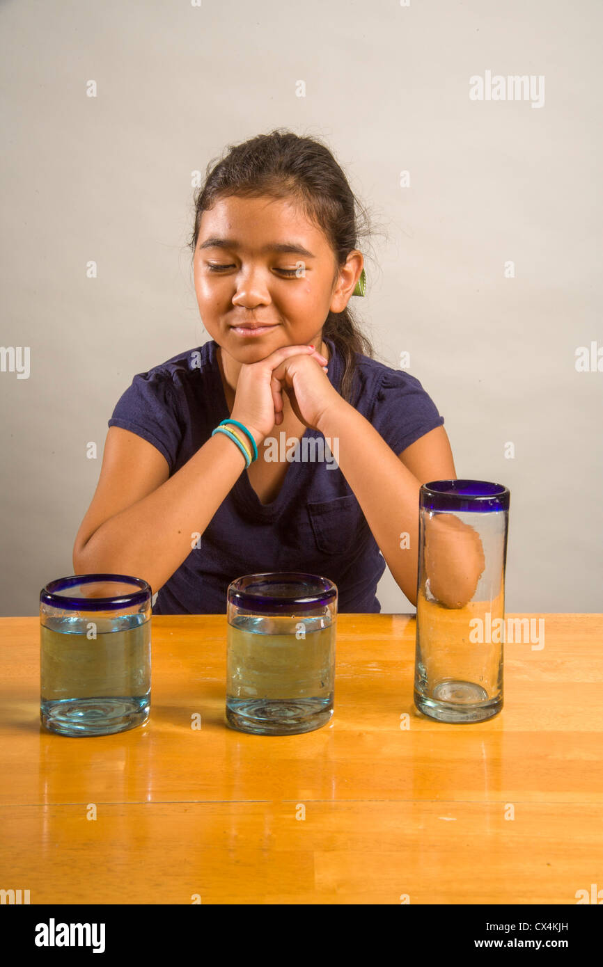 Un enfant regarde verres identiques remplis de la même quantité de liquide à démontrer l'expérience de Piaget Conservation liquide. Banque D'Images
