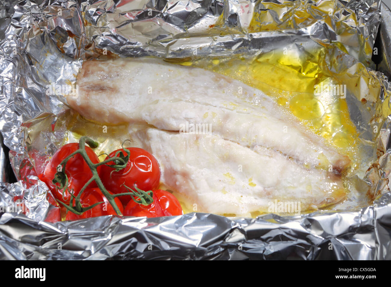 Un filet de poisson blanc et un brin de tomates cerises cuites avec du beurre dans du papier aluminium. Banque D'Images