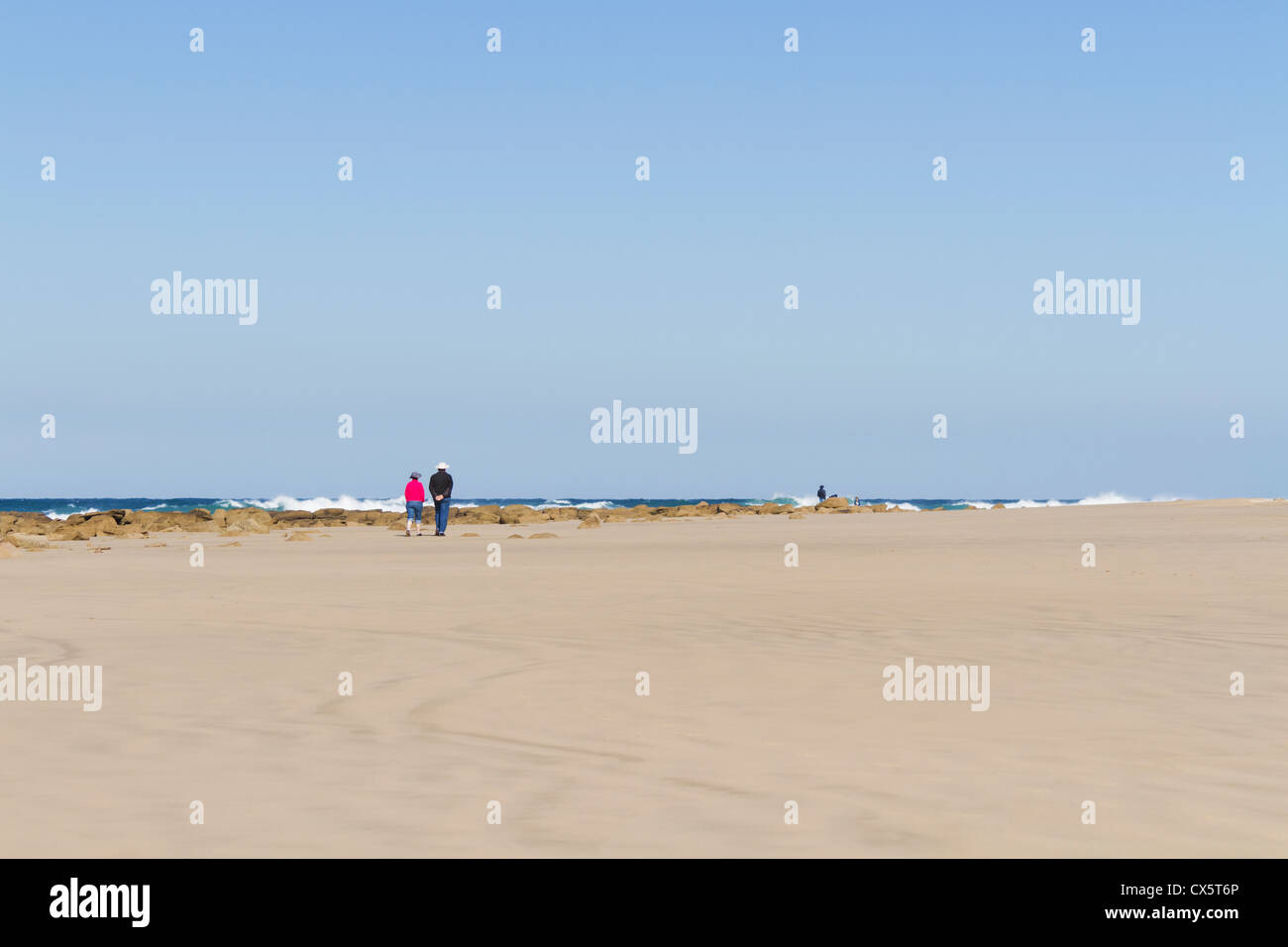 Un couple en train de marcher sur la plage rose et noir Polar Fleece (polaire, Jersey) , Jean bleu, blanc chapeau avec un ciel bleu Banque D'Images