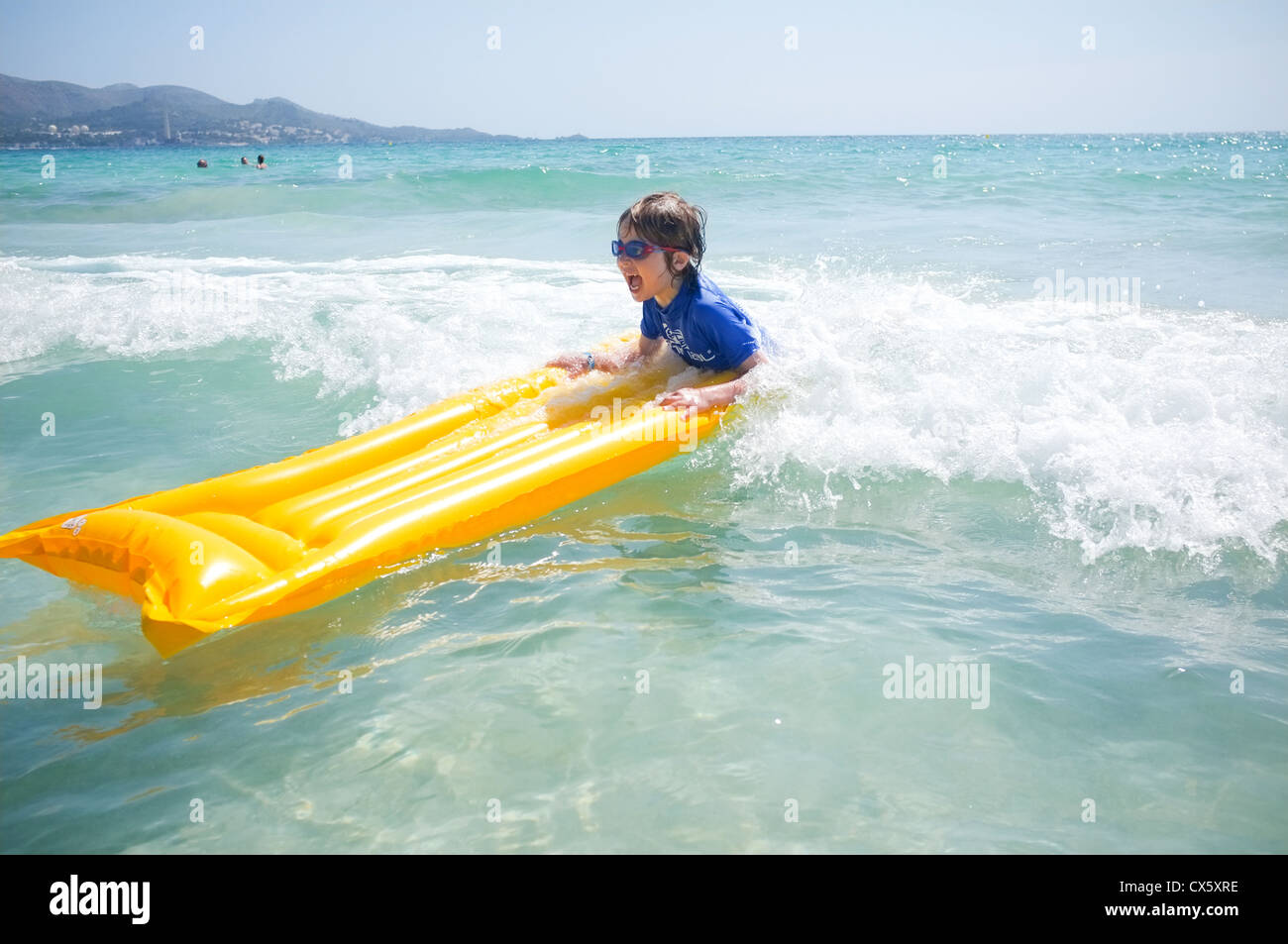 Un jeune garçon joue sur un radeau gonflable lilo dans les vagues sur une plage ensoleillée Banque D'Images