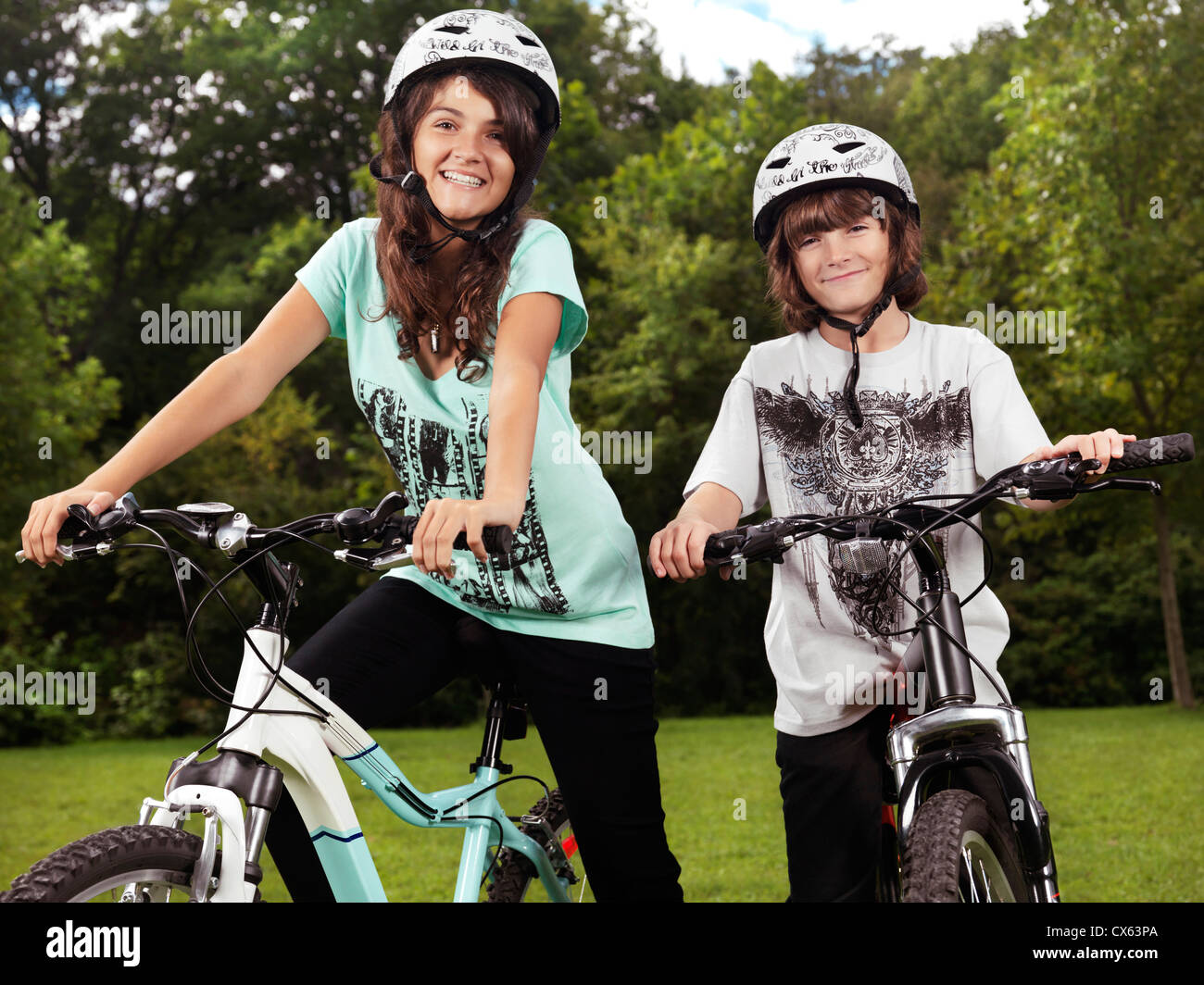 Deux heureux enfants souriants en cyclisme casques sur leur bicyclette dans un parc, frère et sœur, 10 et 13. Banque D'Images