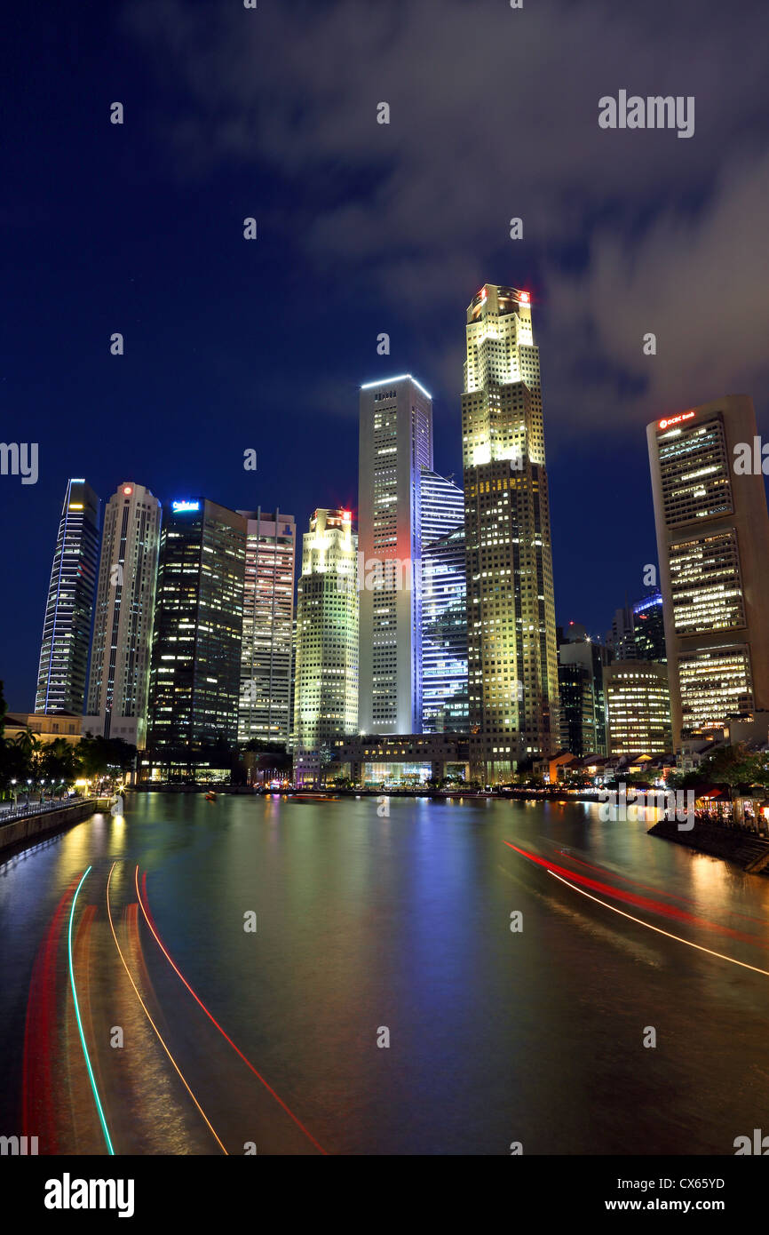 Light trails de barques sur la rivière Singapour avec des immeubles de grande hauteur du centre-ville de Singapour dans l'arrière-plan. Banque D'Images