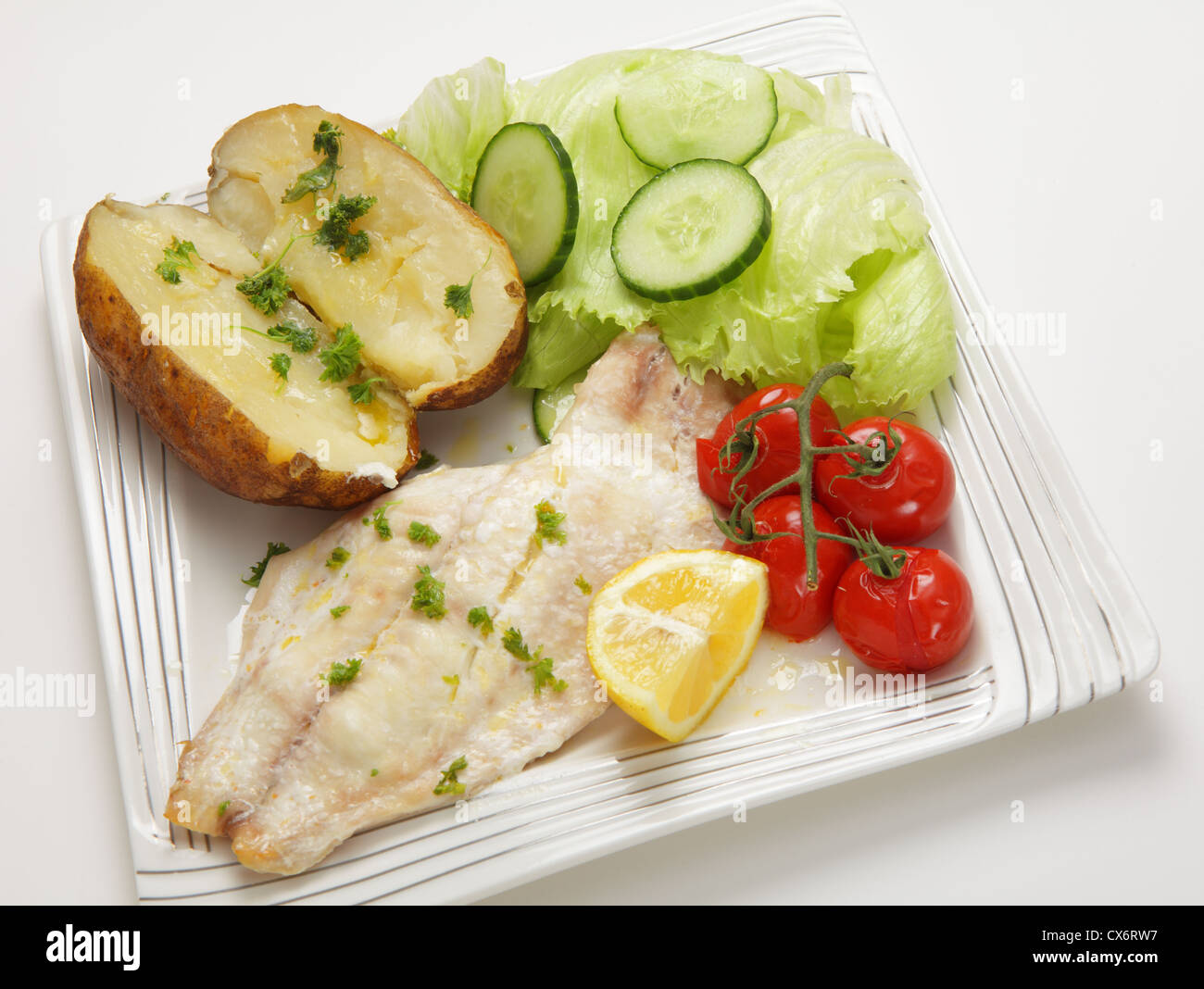 Gros plan sur un filet de poisson blanc cuit au four servi avec une pomme de terre et les tomates, une pointe de citron et une salade Banque D'Images