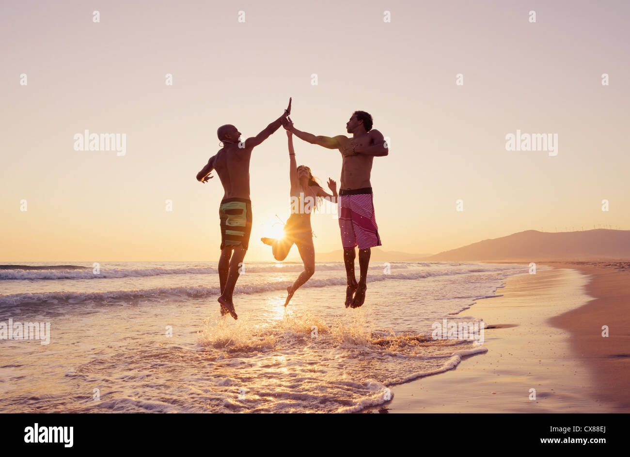 Trois personnes sautant en l'air pour frapper les mains ensemble sur une plage au coucher du soleil ; Tarifa, Cadix, Andalousie, Espagne Banque D'Images