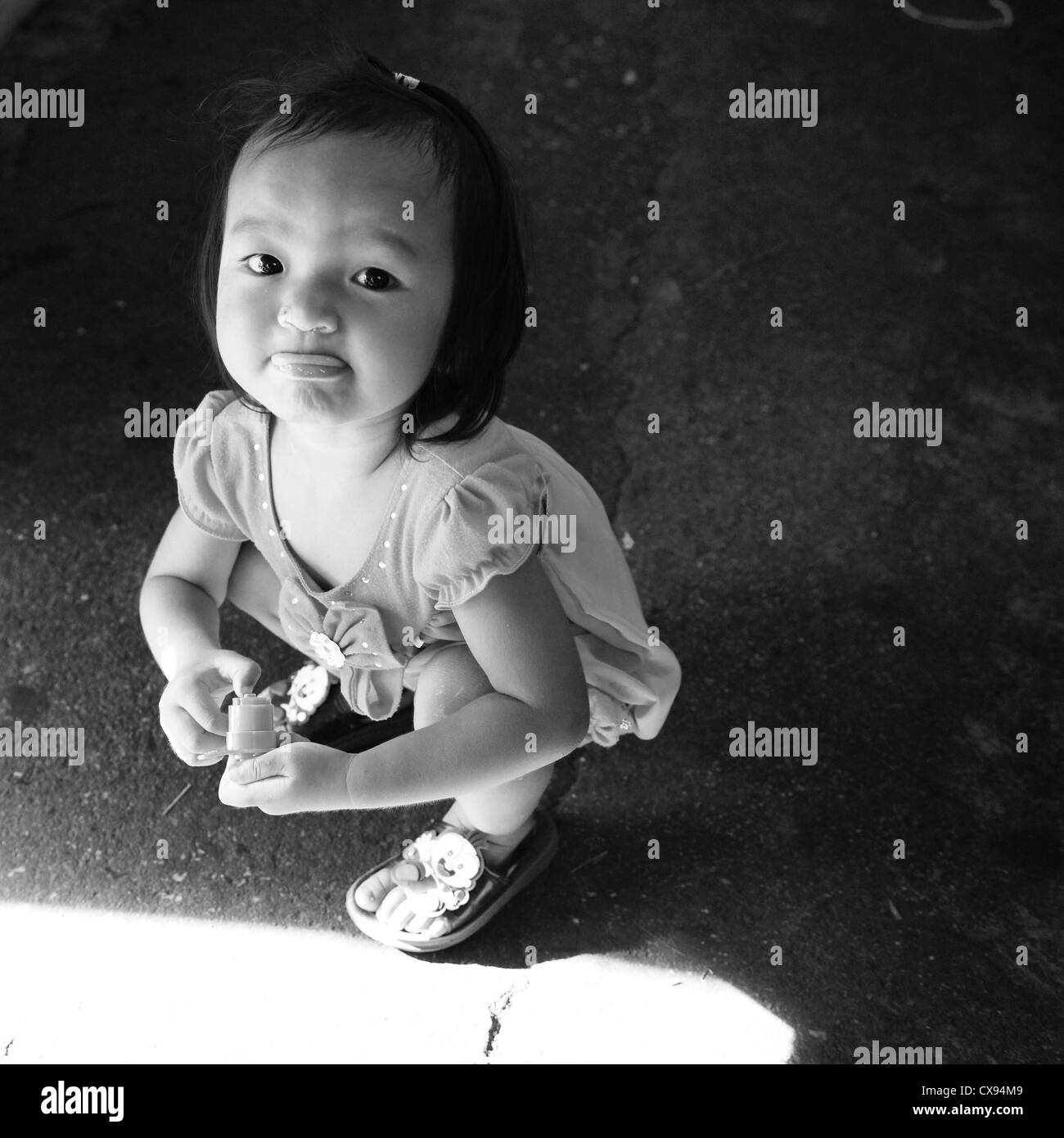 Jeune fille thaïe accroupis sur le béton en noir et blanc Banque D'Images