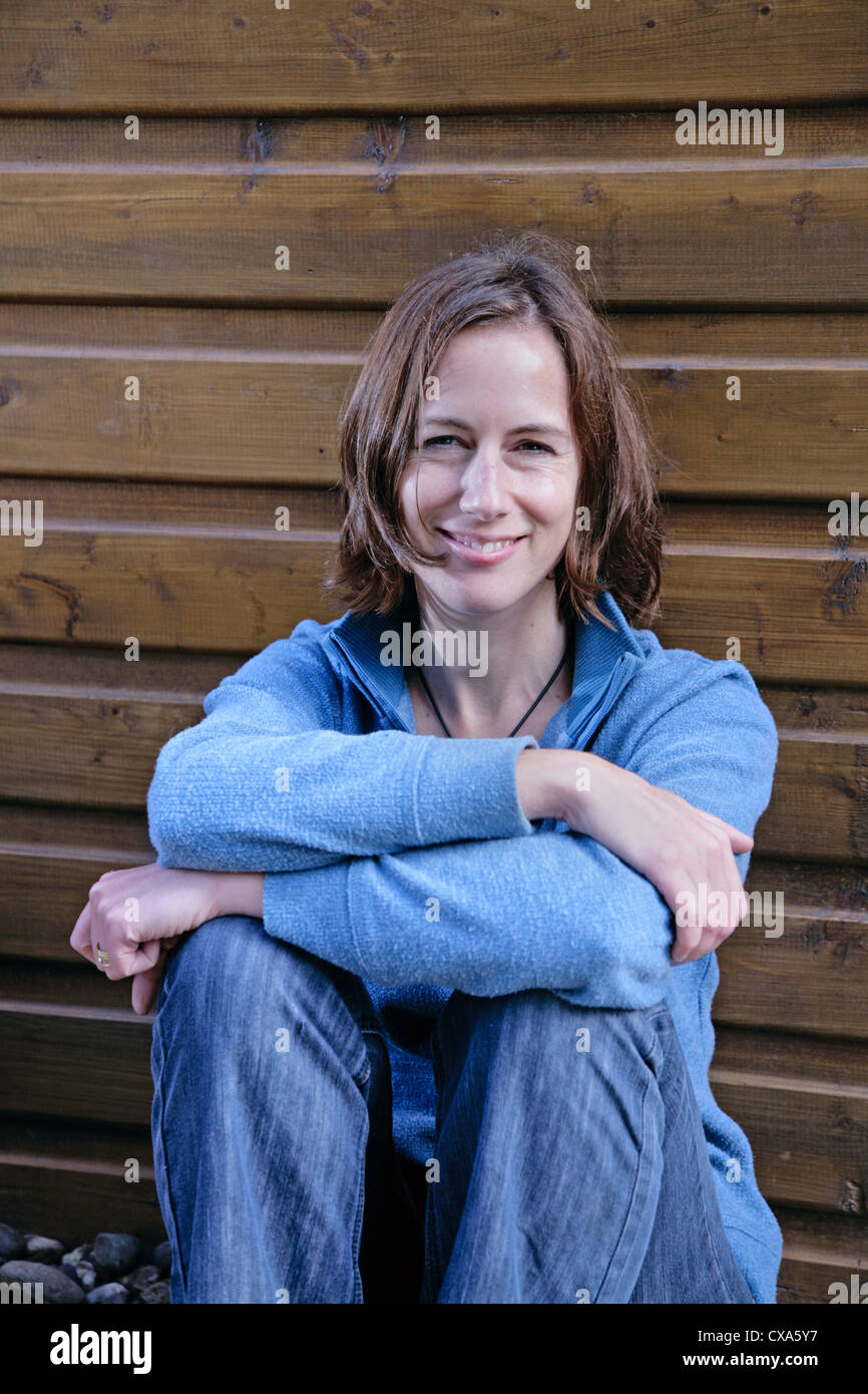Happy young woman leaning against a wooden wall Banque D'Images