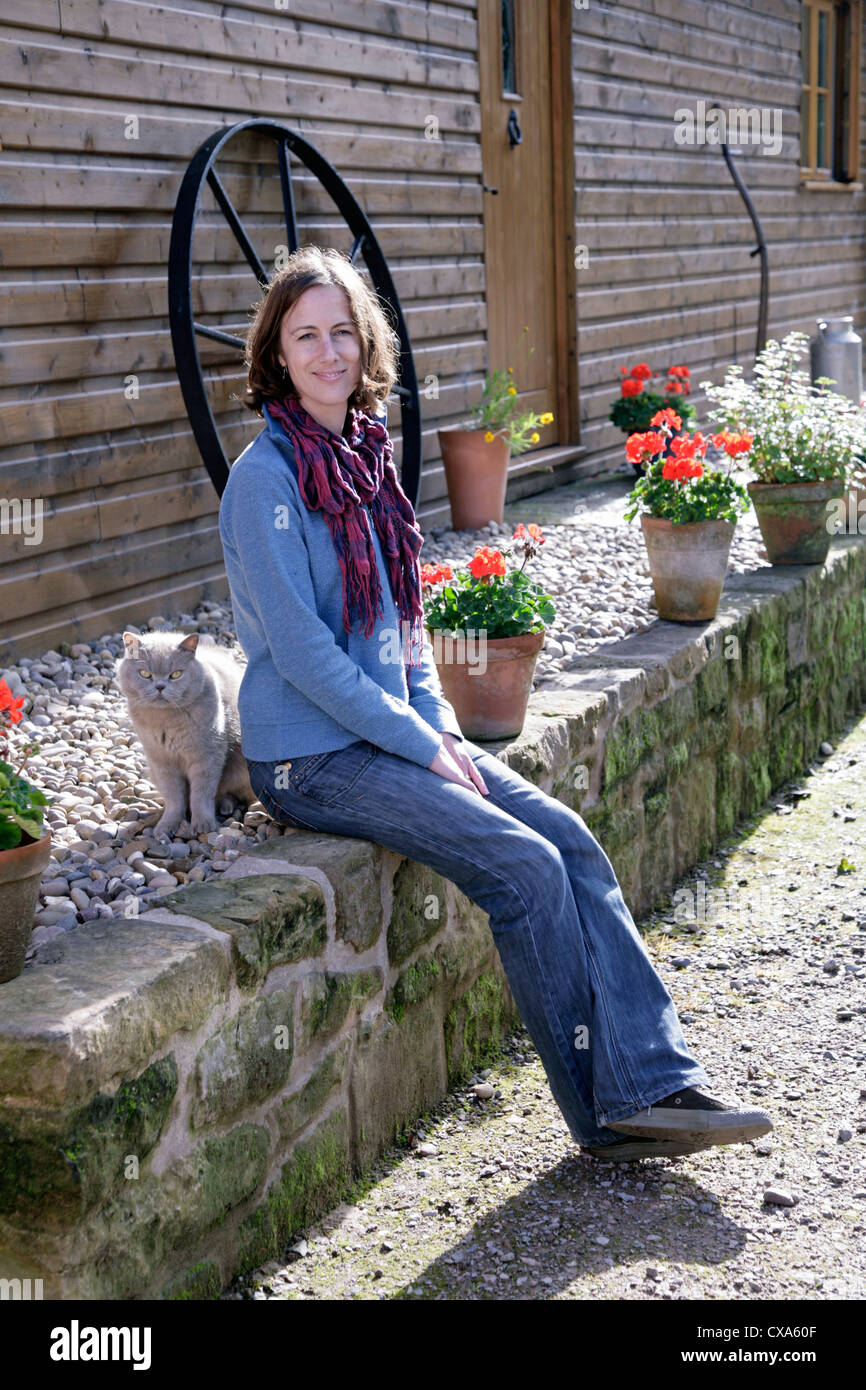 Jeune femme assise sur un mur avec un chat domestique Banque D'Images