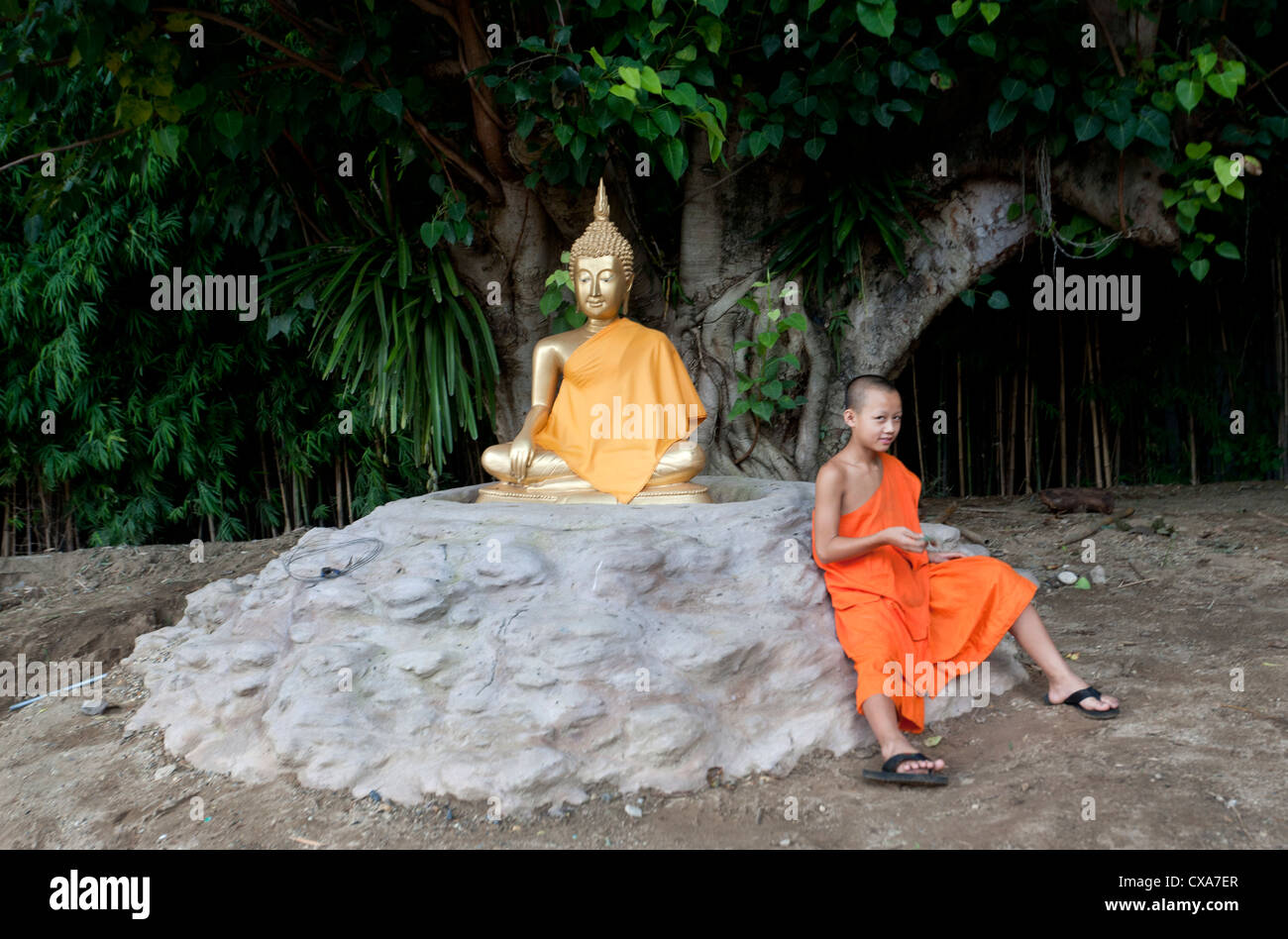 Jeune novice assis près d'une statue de Bouddha de Wat Chet Lin temple Chiang Mai Thailand Banque D'Images