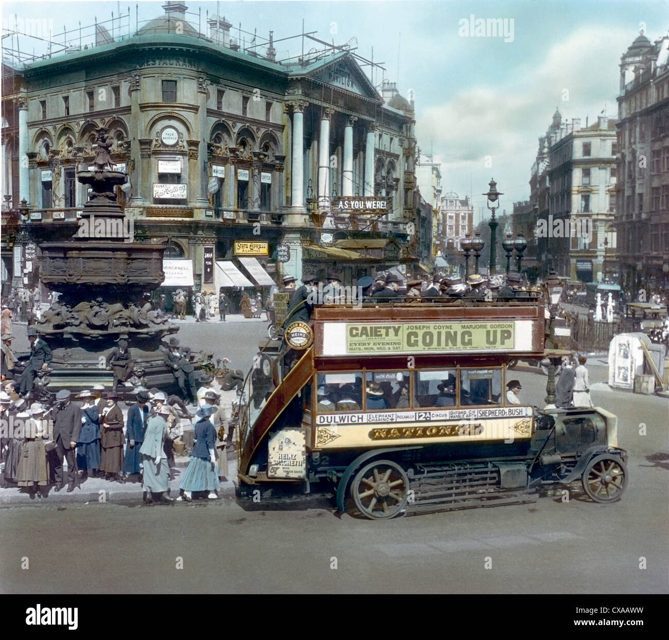 Vue colorée d'une scène de rue à Piccadilly Circus, Londres, 1919. Les passagers montent à bord d'un bus à impériale à côté de la fontaine du Mémorial de Shaftesbury, sur laquelle la statue d'Eros a été enlevée. Le pavillon de Londres est vu en arrière-plan avec ‘comme vous étiez’ affiché sur le chapiteau. (Photo de Burton Holmes) Banque D'Images
