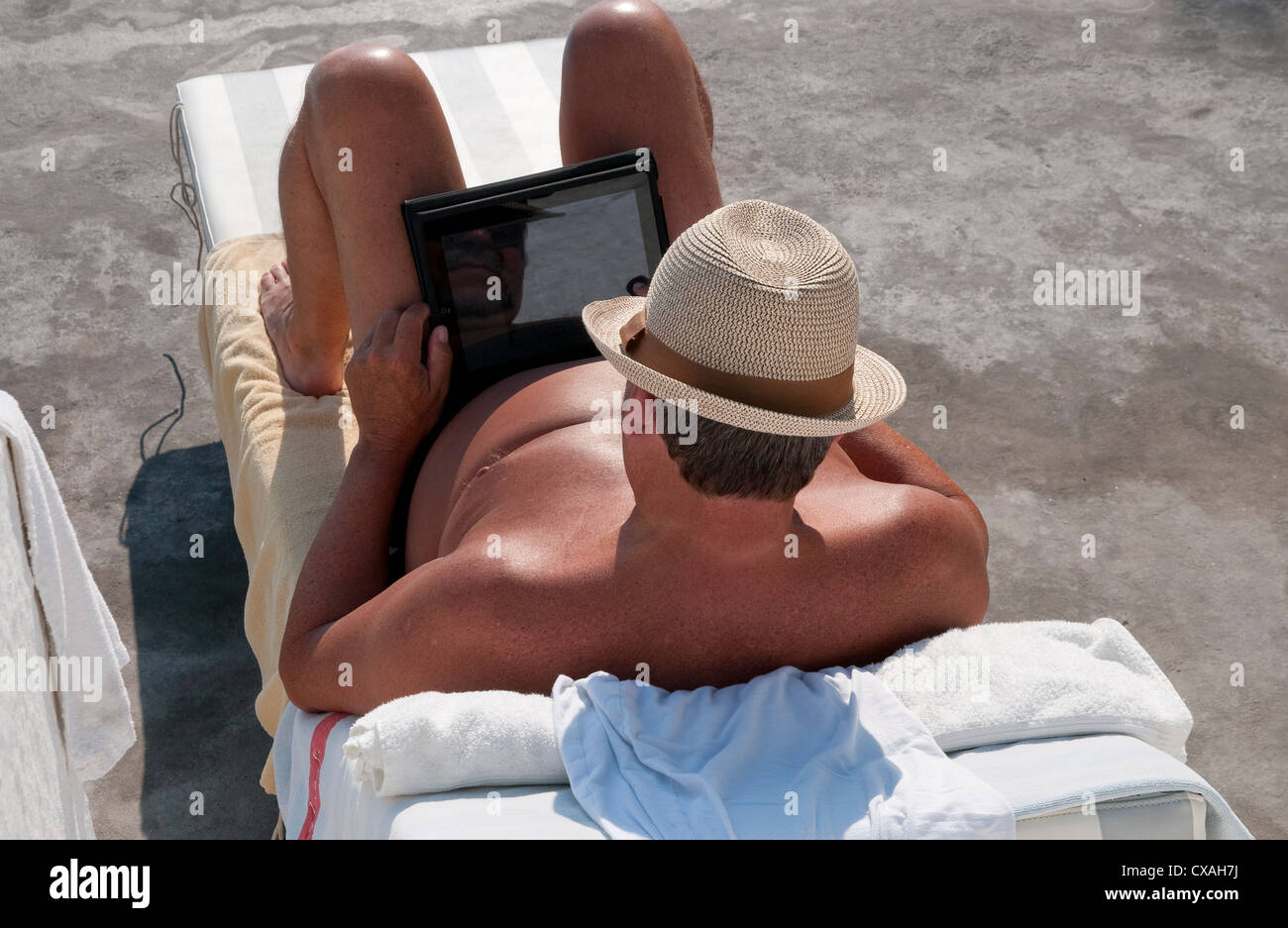 L'utilisation de l'ipad vacancier mâle ordinateur sur lit de soleil, Santorini, Grèce Banque D'Images
