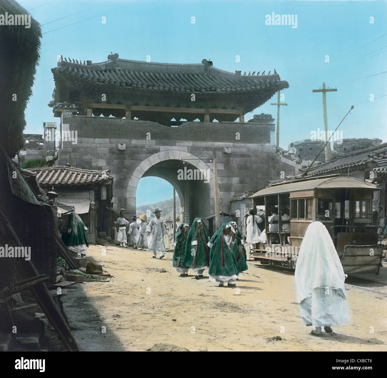 Photo colorisée d'une scène de rue à côté de la porte Donuimun, également connue sous le nom de porte Ouest, Séoul, Corée, 1899. Un tramway approche de la porte et des piétons, y compris des femmes enveloppées dans des capes, marchent dans les deux directions (photo de Burton Holmes) Banque D'Images