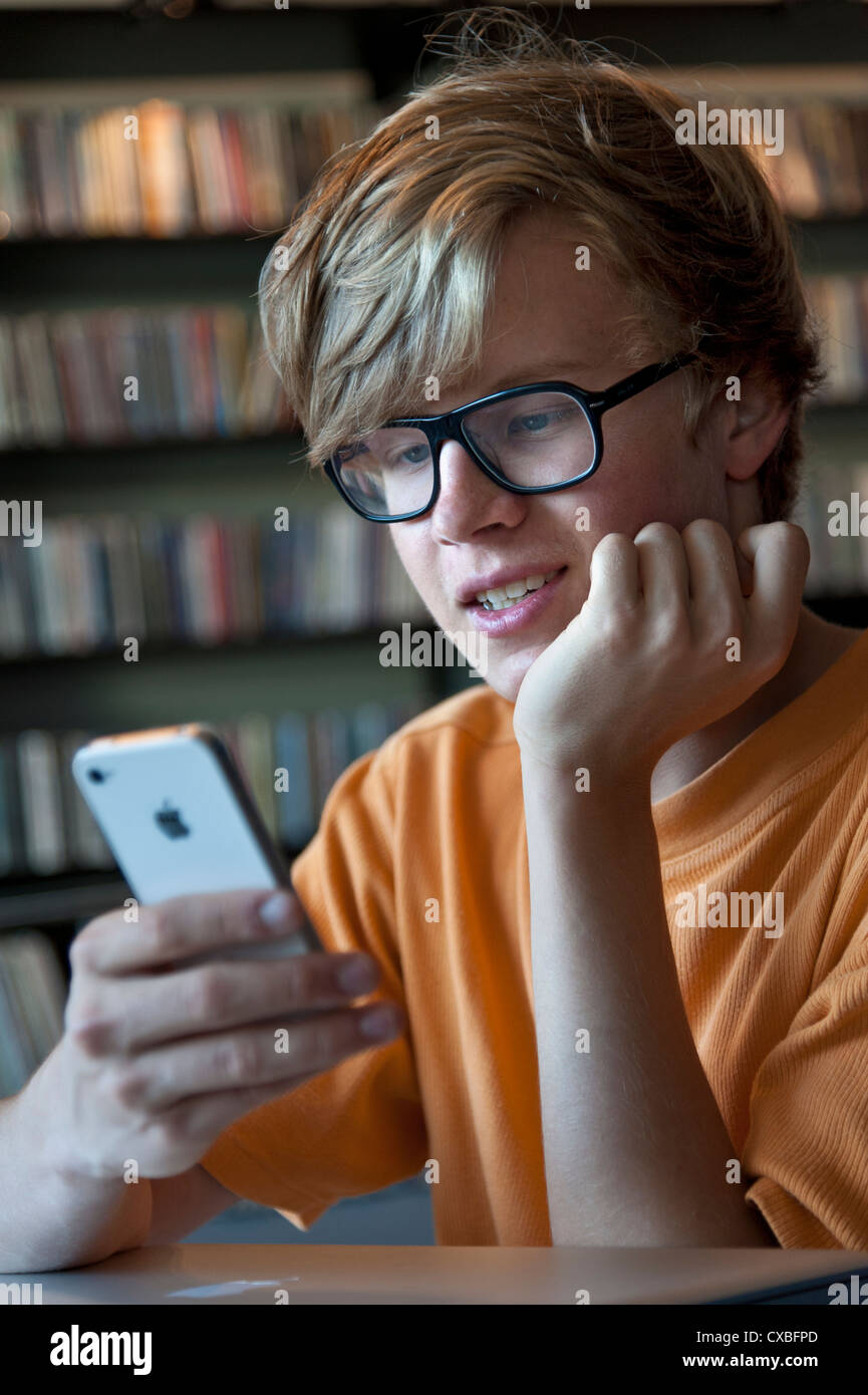 Professionnels attrayants en écolier studieux teenage music library en utilisant son Smartphone Apple iPhone 4s Banque D'Images