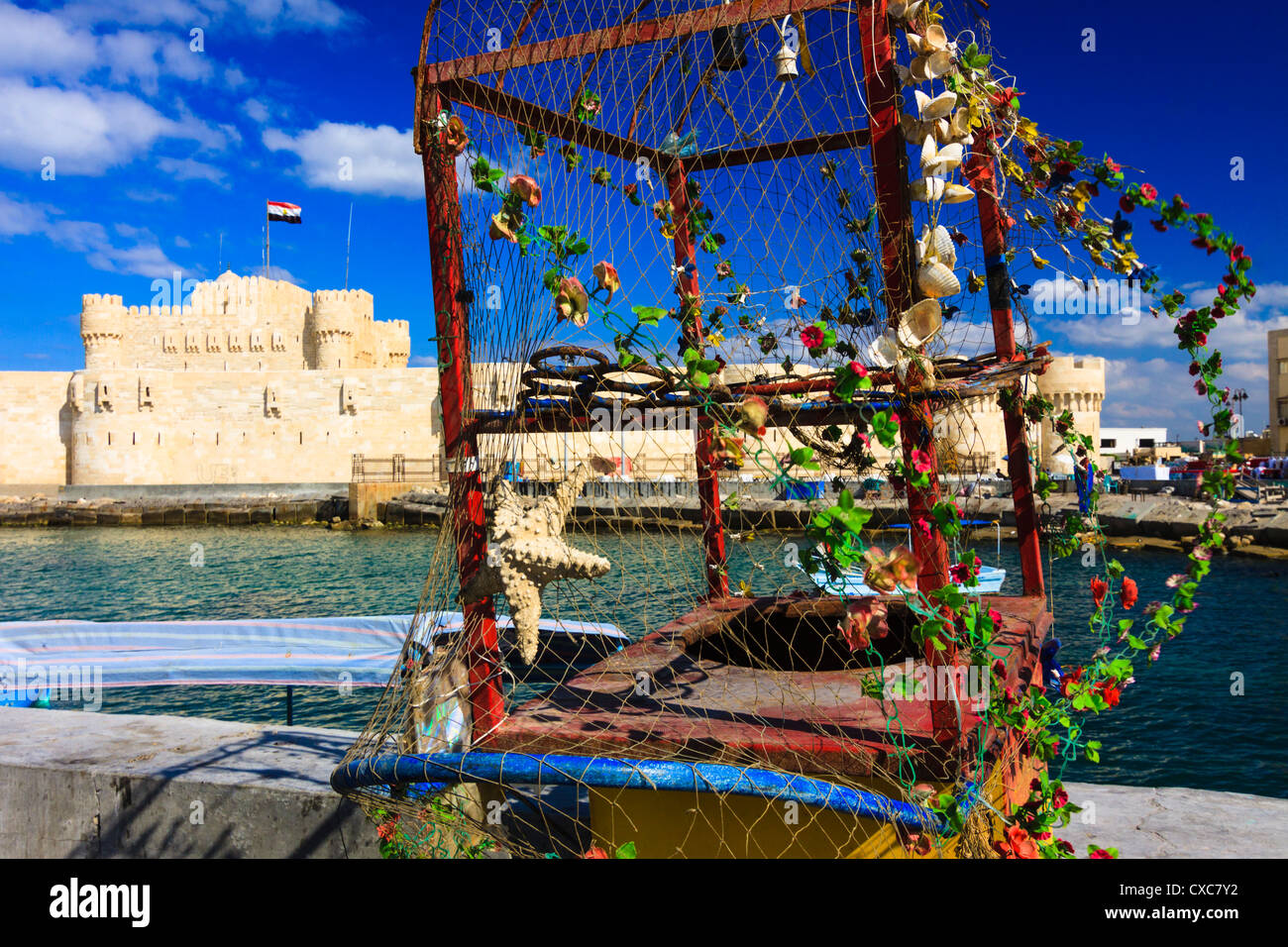 Fort Qaitbey avec chariot coloré vide avec des étoiles de mer, coquillages et fleurs en premier plan. Alexandria, Egypte Banque D'Images