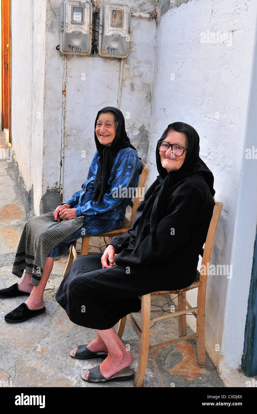 Deux vieilles dames s'assoient à l'extérieur de leurs maisons et parlent dans une allée ombragée, loin des intenses températures de Junes à Pano Elounda, en Crète, en Grèce Banque D'Images