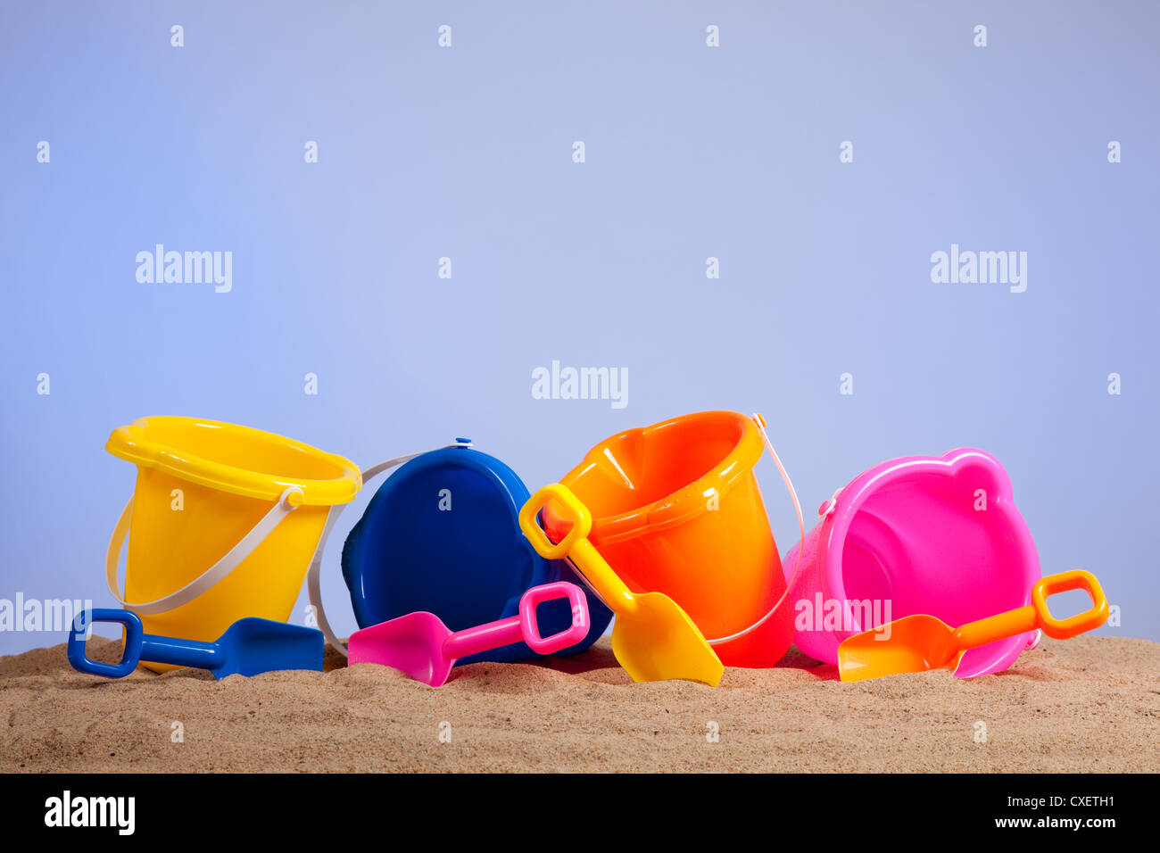 Une ligne de plage multicolores seaux ou des seaux avec des pelles sur une plage de sable fin avec blue sky background with copy space Banque D'Images