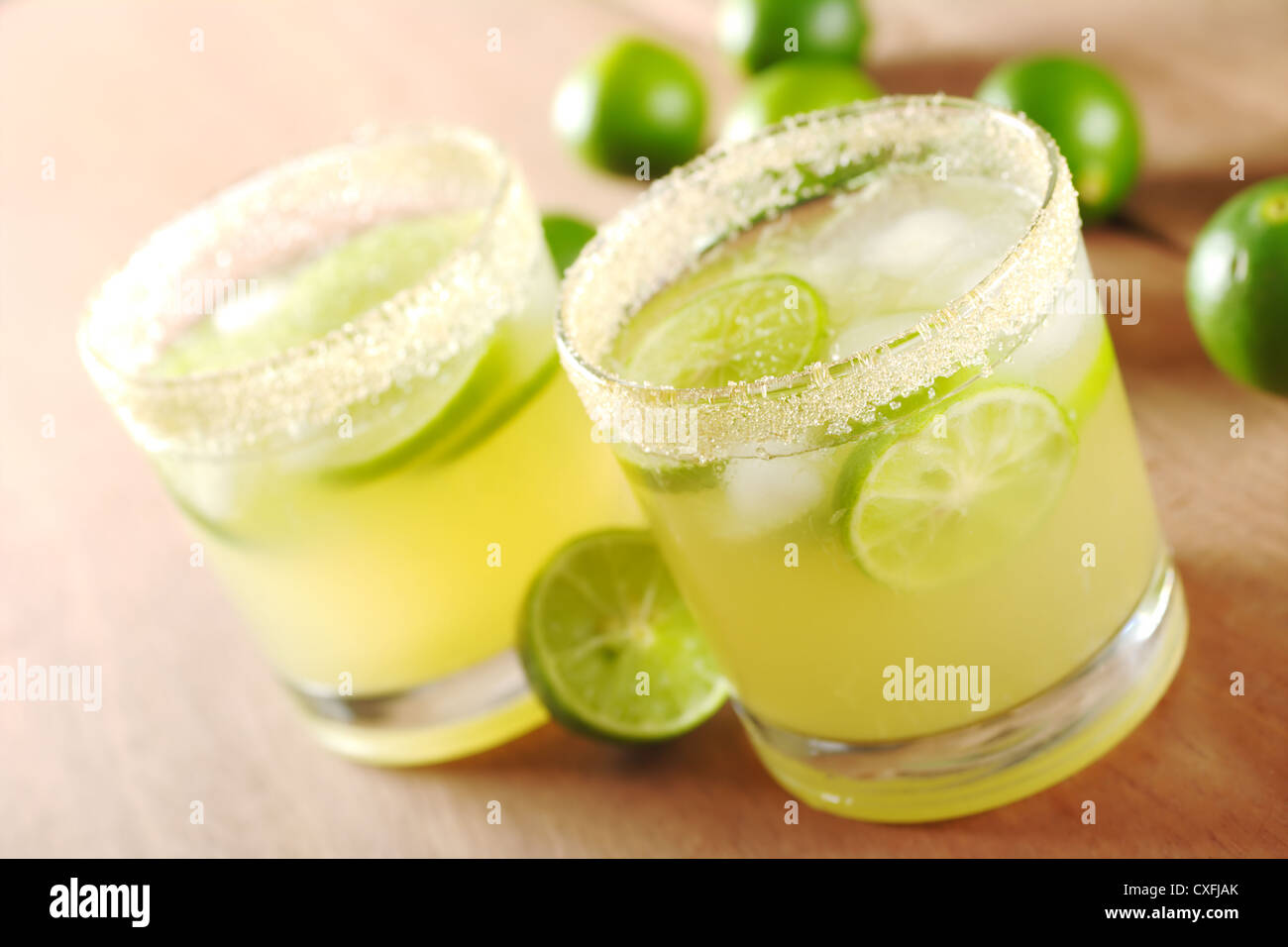 Limonade Fraîche avec des tranches de citron vert et des glaçons dans un verre à rebord sucre entouré de limes sur bois Banque D'Images