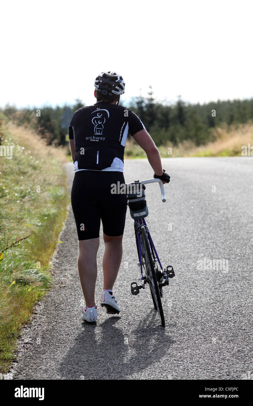 Cycliste route en poussant son vélo en haut d'une colline, dans l'Aberdeenshire, Scotland, UK, un jour ensoleillé tourné par derrière avec vue arrière montrant Banque D'Images