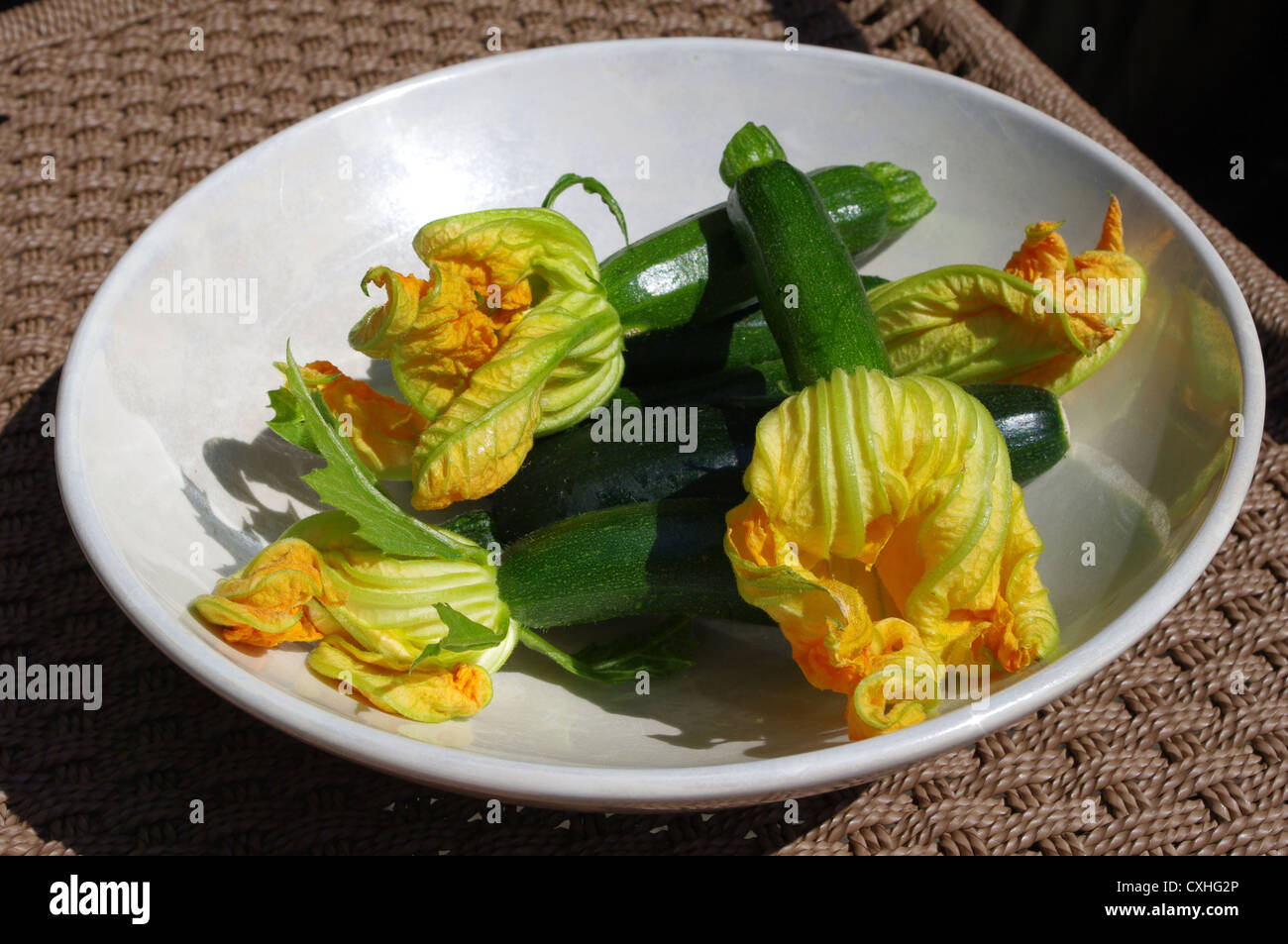 Courgettes avec leurs fleurs sur un brillant blanc bol. Derrière l'effet d'osier. Banque D'Images Courgettes avec leurs fleurs sur un brillant blanc bol. Derrière l'effet d'osier. Banque D'Images