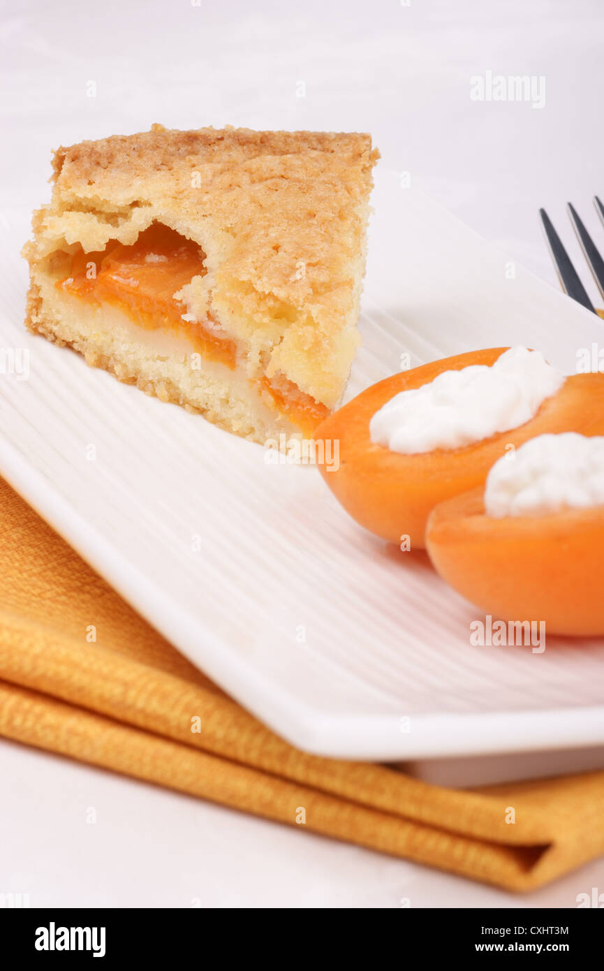 Tranche de Tarte aux abricots servi sur une plaque blanche. Les abricots en tranches avec la crème fouettée n'est pas mise au point en avant-plan Banque D'Images