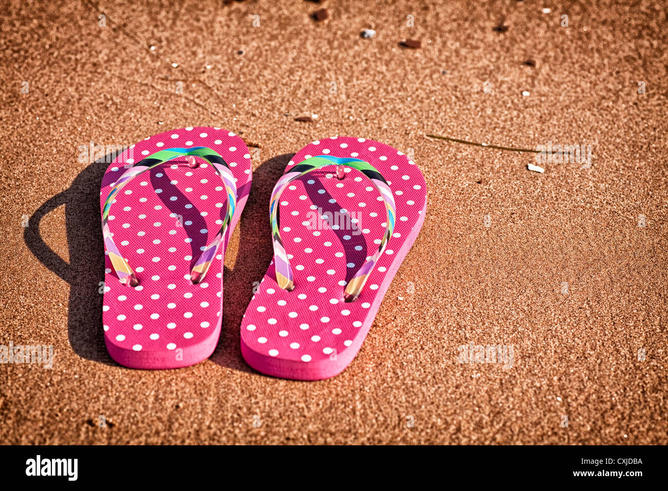 Pink polka dotted tongs sur la plage. Banque D'Images