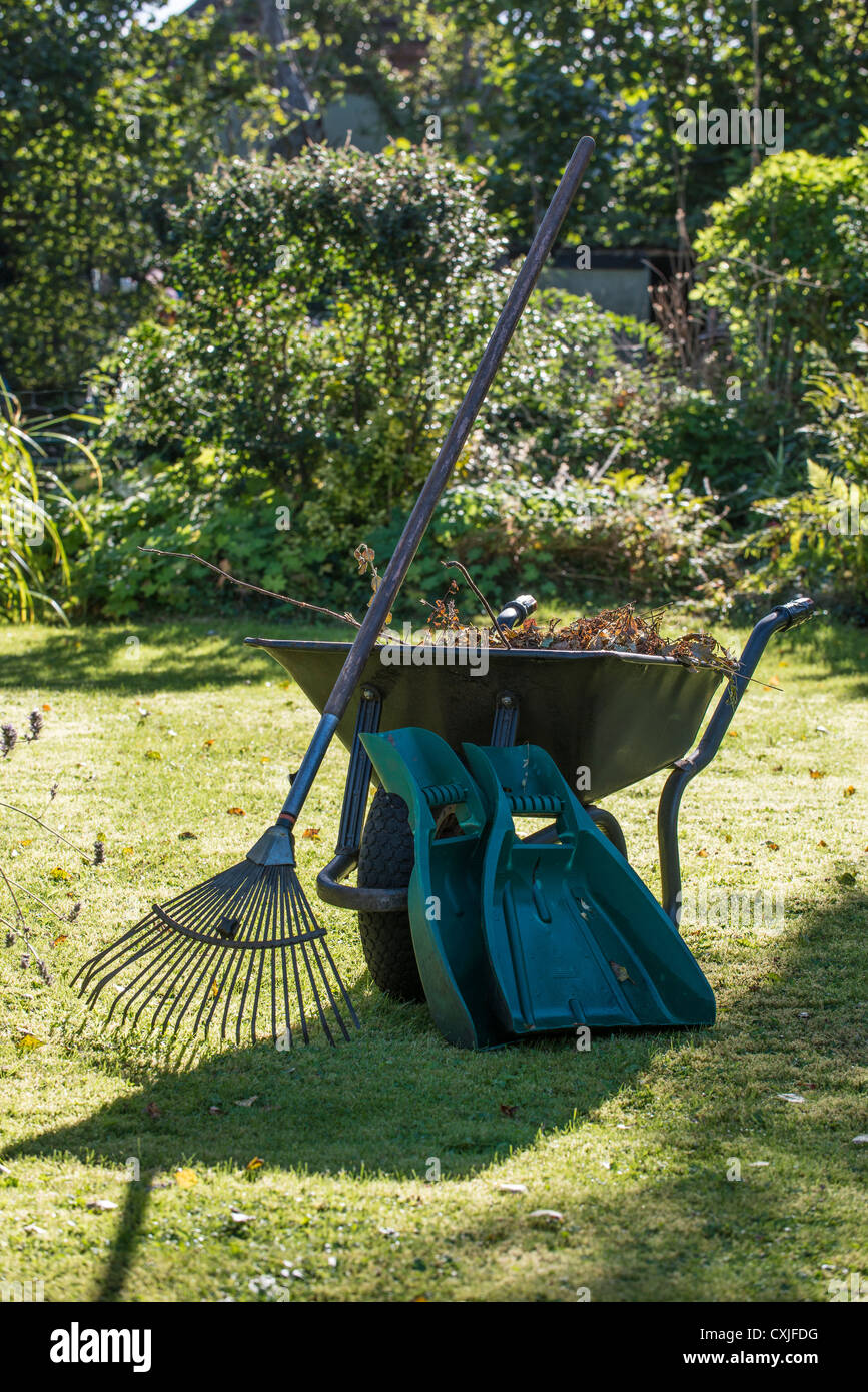 Brouette pleine de déchets de jardin/débris avec le râteau et collectionneurs de feuilles à la fin de l'été/début de l'automne jardin. Gloucestershire UK Banque D'Images