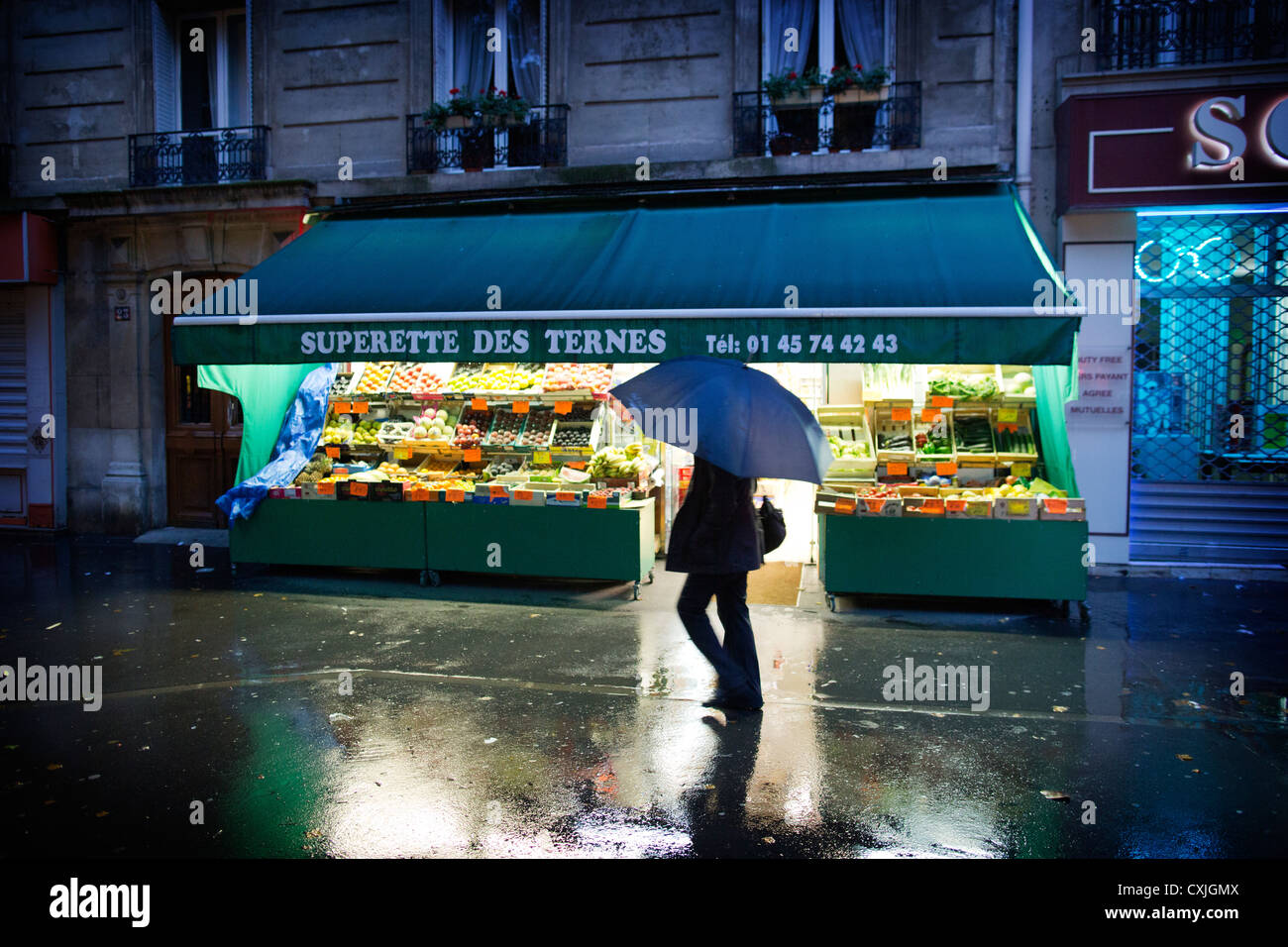 Scène de rue, une personne marchant sous la pluie après un petit mini-marché local à Paris France Superette des Ternes Banque D'Images