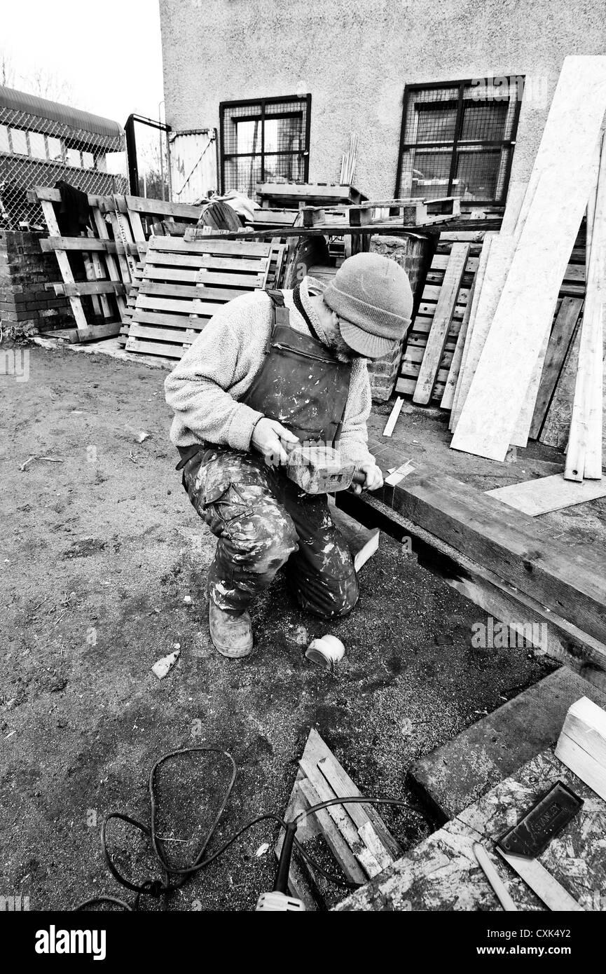 L'homme sur un terrain boueux à l'aide d'un site de construction old fashioned maillet en bois et d'un burin. Banque D'Images