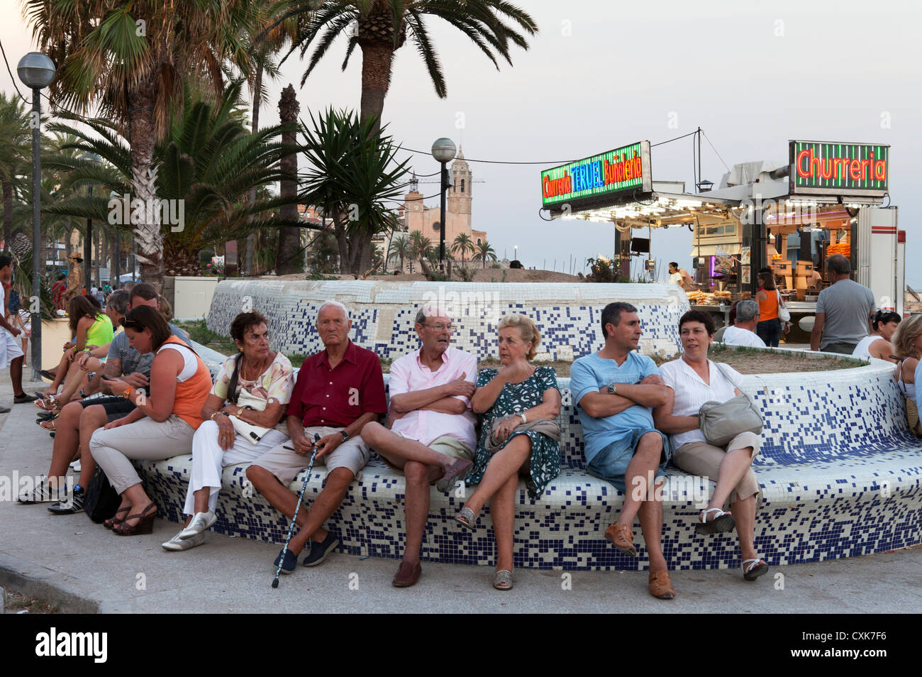 Les aînés de la région et les touristes s'asseoir sur un banc le long de la promenade de la plage dans Sitges, Espagne, au crépuscule. Banque D'Images