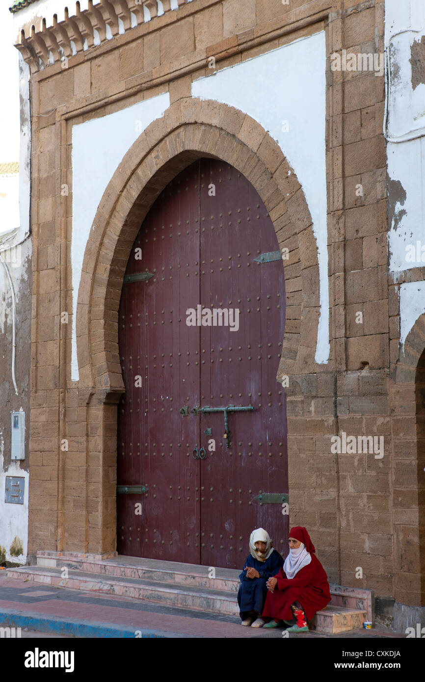 Deux femmes marocaines assis à parler sur l'étape par la grande porte en bois, Essaouira, Maroc Banque D'Images