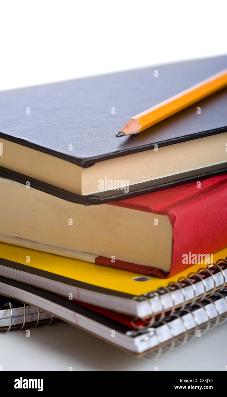 Une pile de livres scolaires et d'ordinateurs portables en spirale avec un crayon et des stylos sur des tops devant un fond blanc Banque D'Images