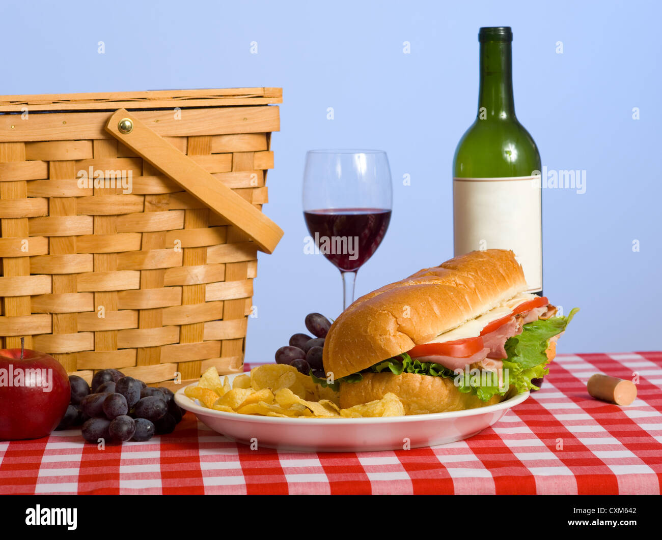 Panier pique-nique en osier et déjeuner sur une nappe vichy rouge avec  sandwich, vin, raisin et une pomme avec un fond bleu ciel Photo Stock -  Alamy