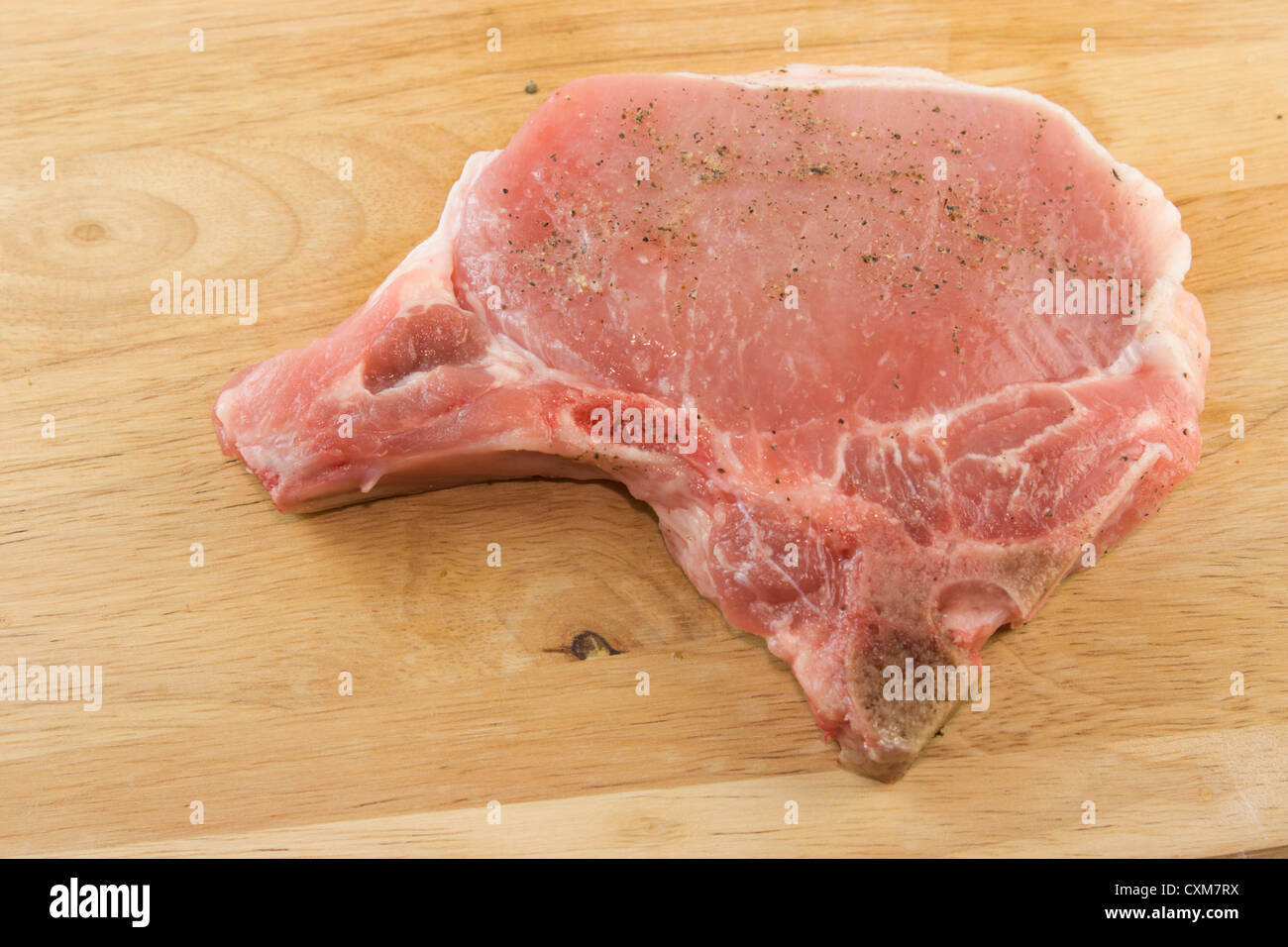 Côtelette de porc frais, assaisonné de sel et de poivre sur une planche à découper en similibois prêt à cuire Banque D'Images