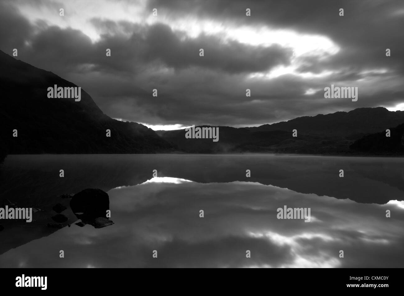 Moody nuages gris reflètent dans l'eau immobile d'un lac, Llyn Dinas, Wales, UK Banque D'Images