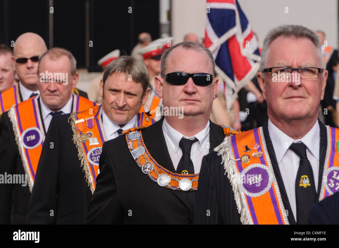 Nombre d'orangistes vêtu du costume traditionnel 'Orange sash' comme ils marchent sur une route pendant une parade de l'ordre d'Orange Banque D'Images