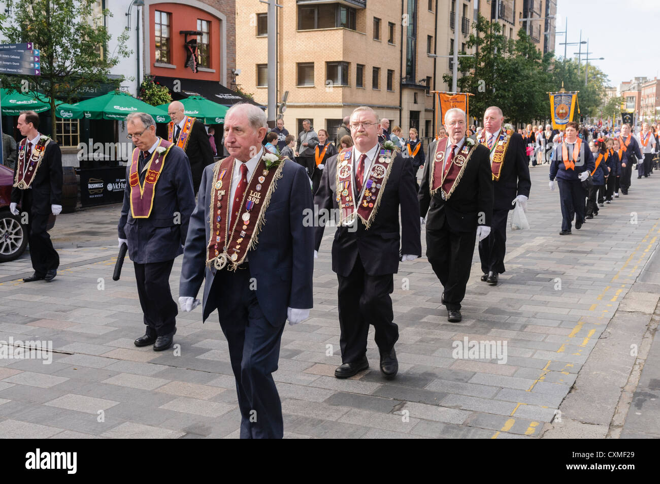 Nombre d'orangistes vêtu du costume traditionnel 'Orange sash' comme ils marchent sur une route pendant une parade de l'ordre d'Orange Banque D'Images