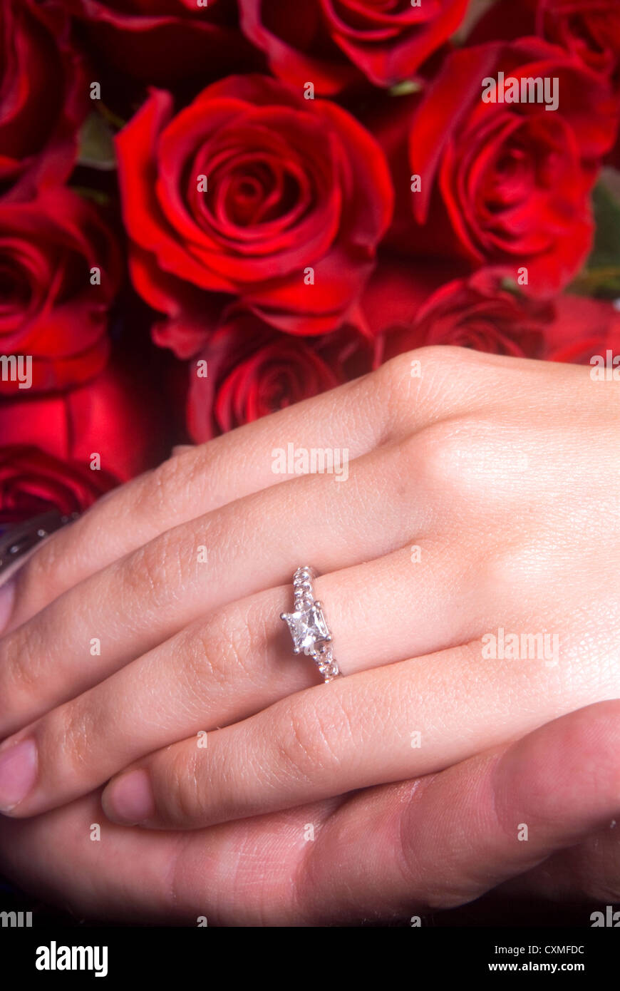 Mari tenant la main de sa femme sur un bouquet de roses montrant sa bague de fiançailles Banque D'Images