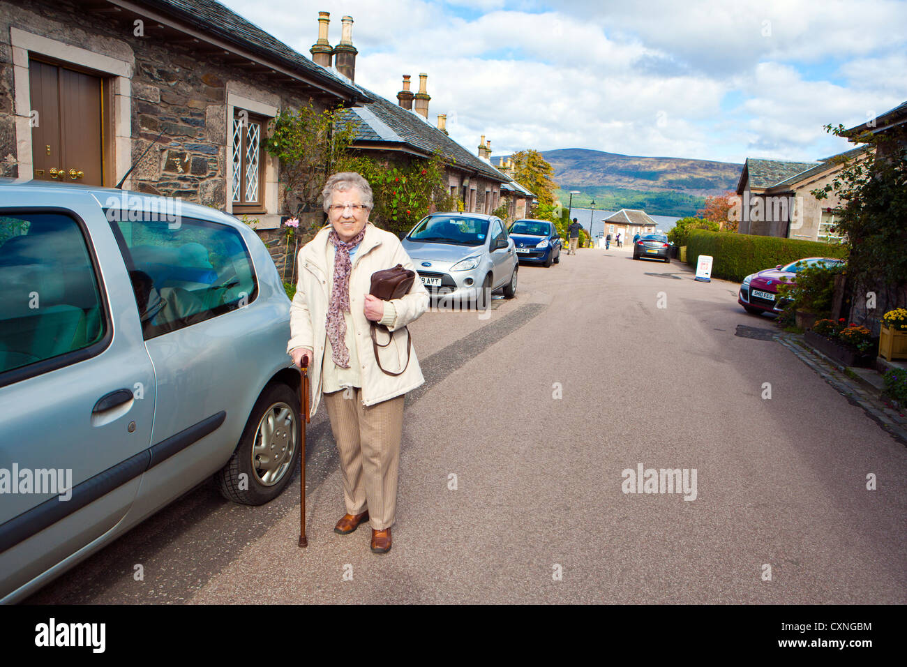 Femme plus âgée marche avec bâton dans le village de Luss Ecosse Banque D'Images