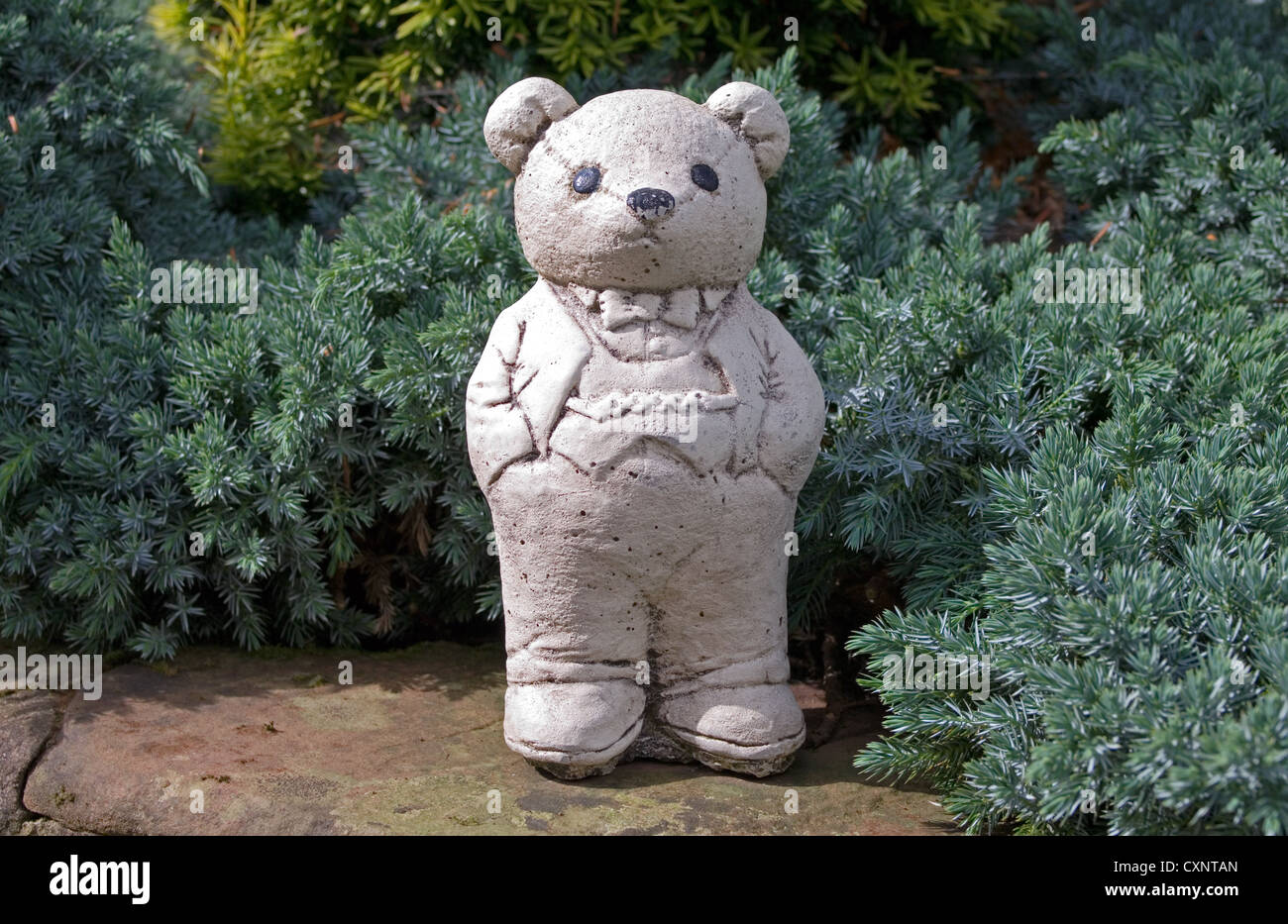 Ornement blanc mignon ours en peluche portant veste et pantalon avec ses mains dans les poches de son pantalon, debout sur le mur du jardin Banque D'Images