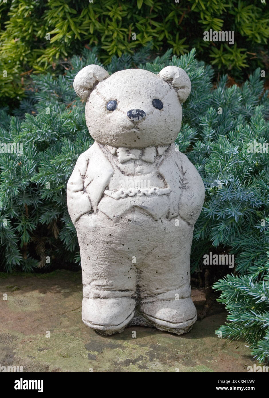 Ornement blanc mignon ours en peluche portant veste et pantalon avec ses mains dans les poches de son pantalon, debout sur le mur du jardin Banque D'Images