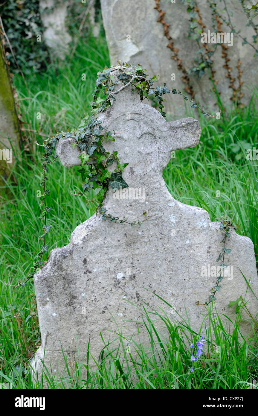 Une vieille croix de pierre tombale en pierre recouvert de lierre dans un cimetière herbeux Banque D'Images