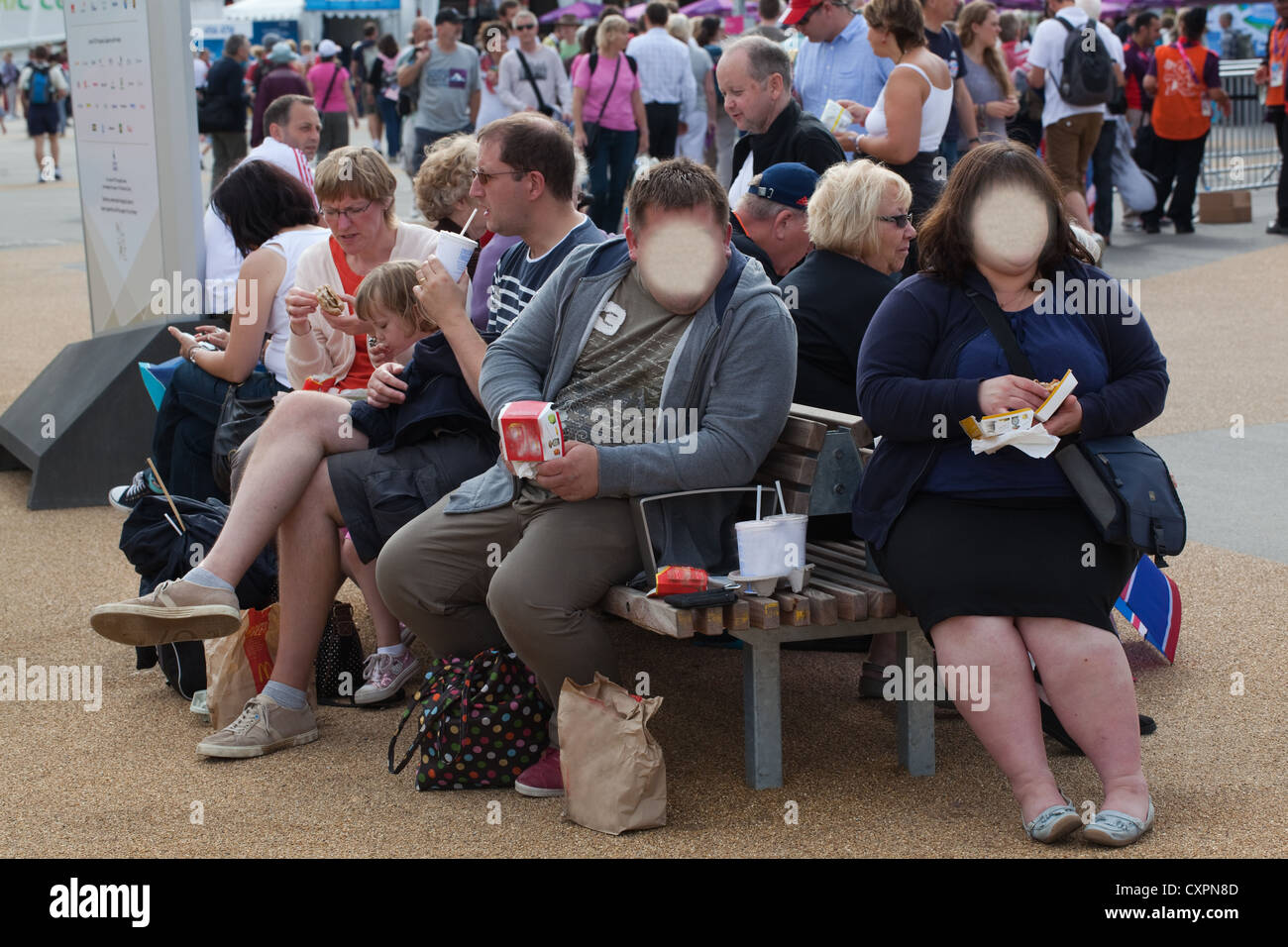 L'homme obèse et Woman eating Junk Food. Londres. L'Angleterre. UK. Les sociétés sises à reconnaître les visages masqués. Banque D'Images