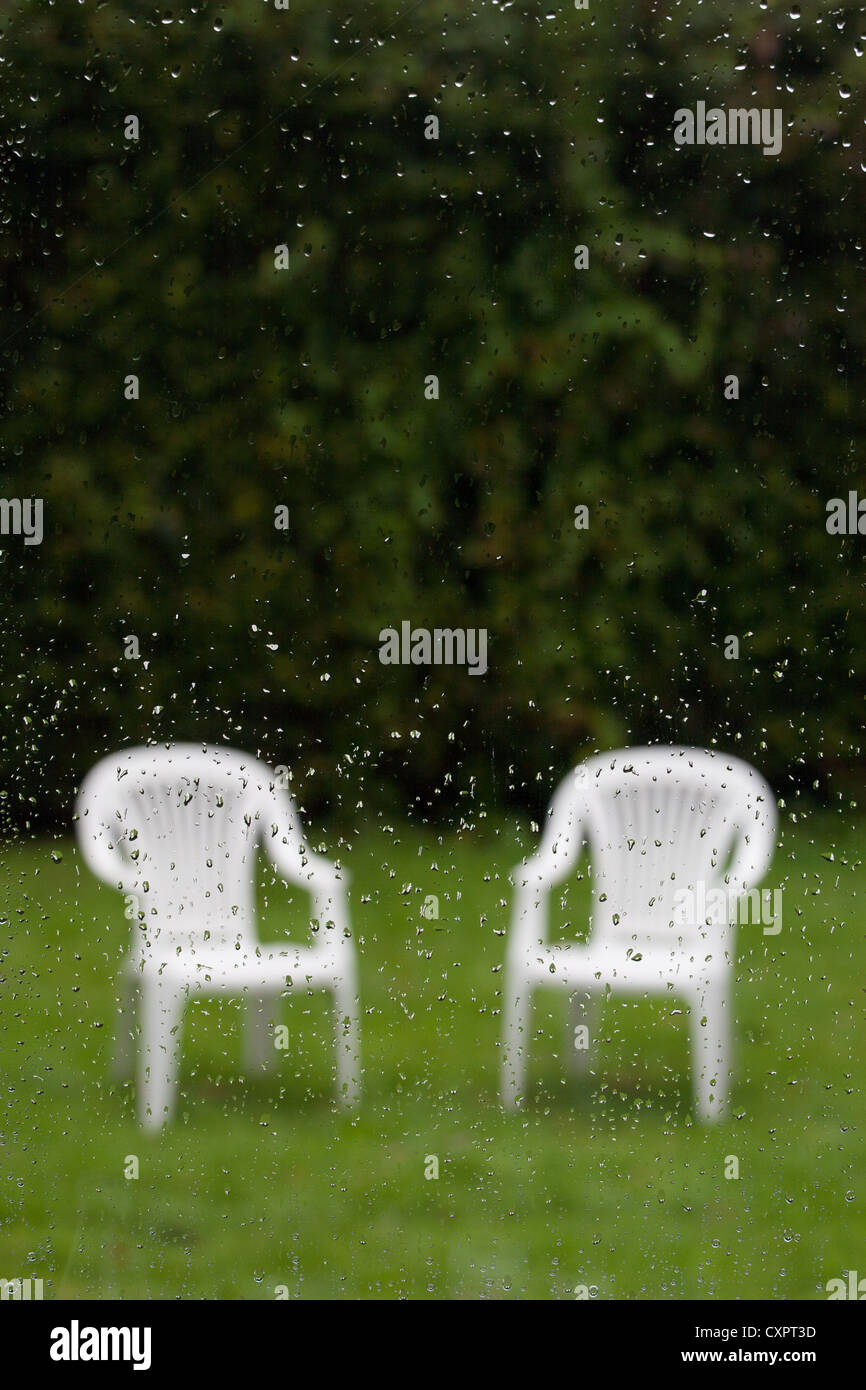 Hors foyer chaises de jardin vue à travers une fenêtre couverte de gouttes de pluie Banque D'Images