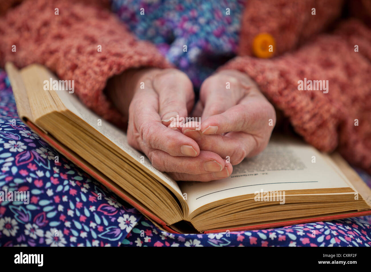 Mains d'une vieille femme allongée sur ses genoux sur un livre ouvert Banque D'Images