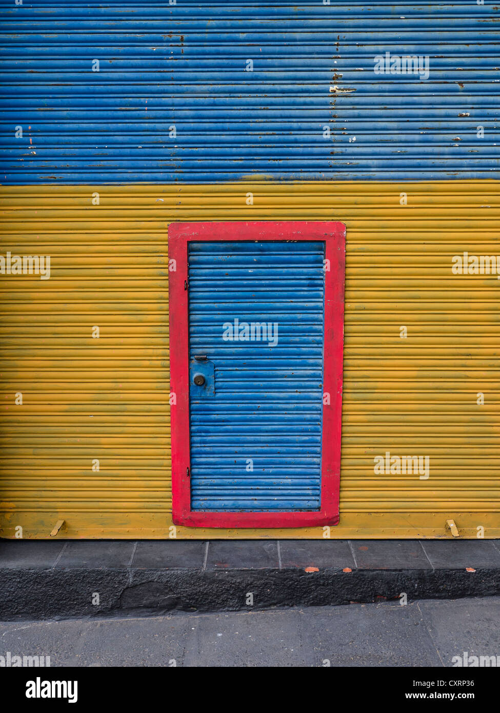 Un mur en carton ondulé peint de couleurs vives, d'un bâtiment en métal avec une porte en métal ondulé avec bordure rouge au centre du mur. Banque D'Images