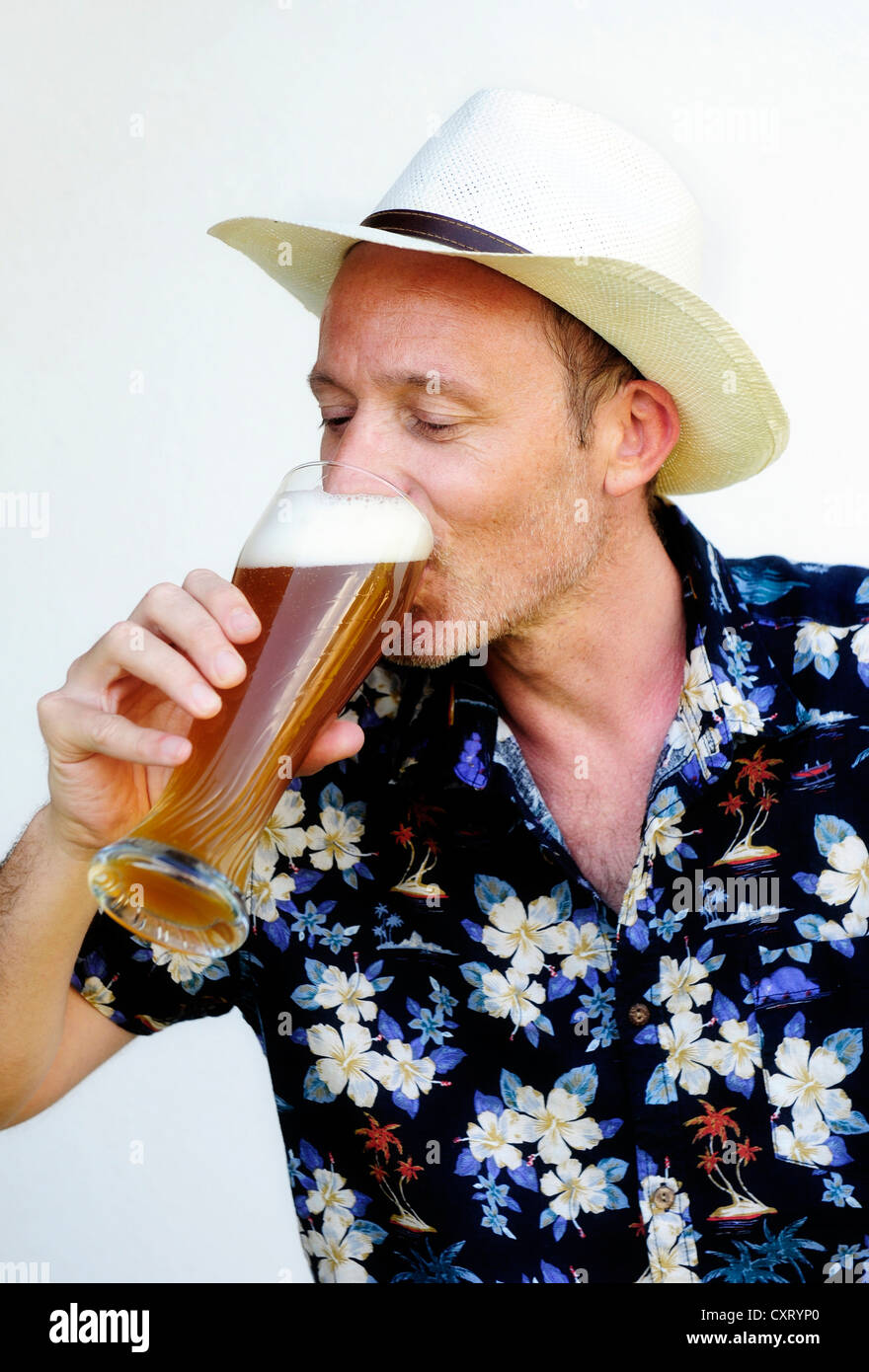 Homme portant un chapeau de paille et une chemise hawaïenne de boire de la bière de froment Banque D'Images