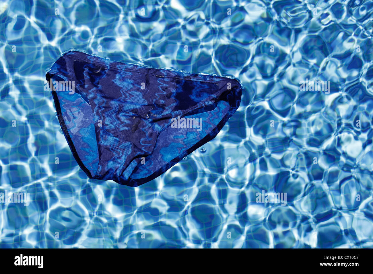 Maillot de bain bleu flottant à la surface d'une piscine extérieure, d'image symbolique pour les vacances ou les jours fériés Banque D'Images