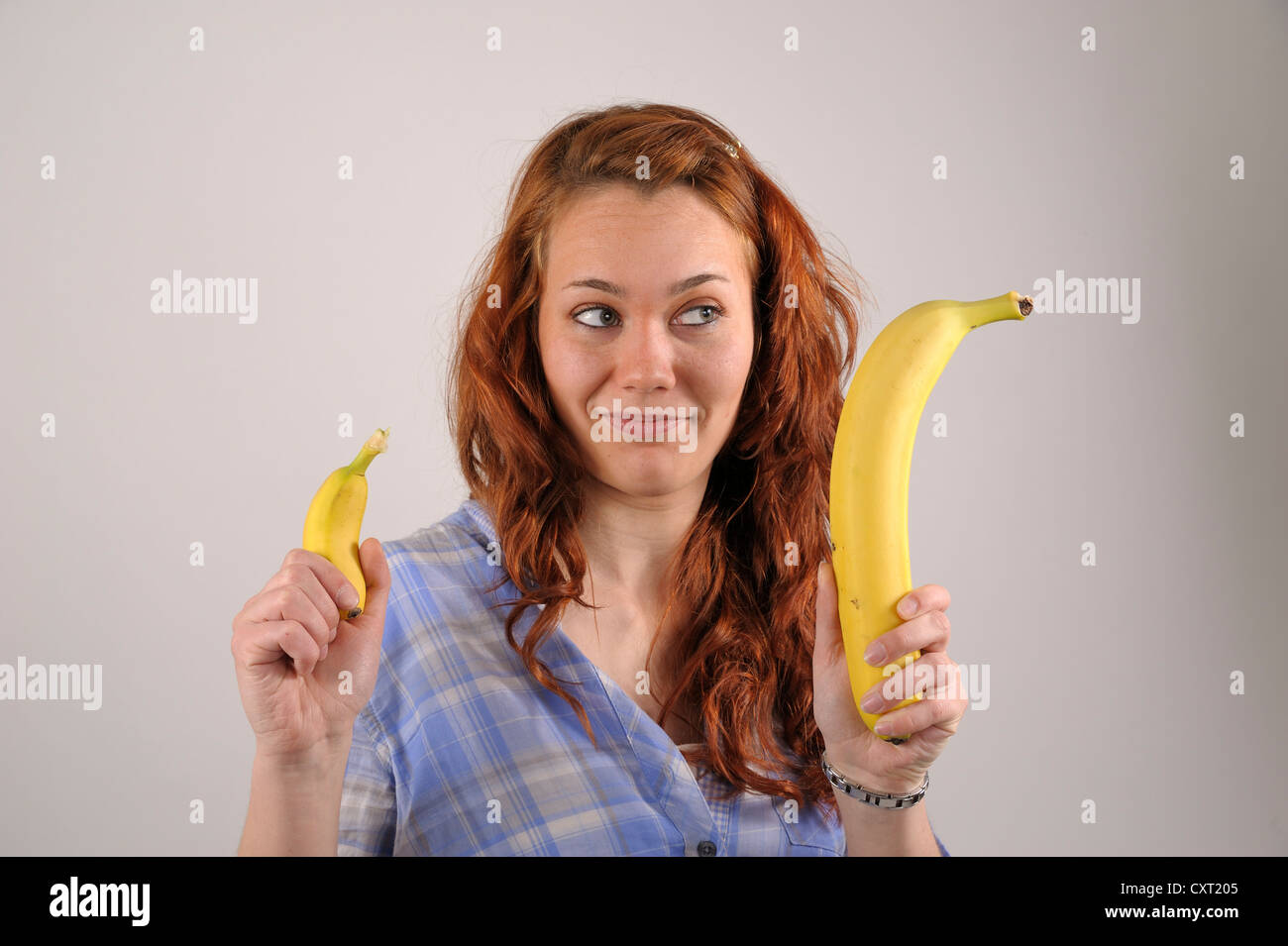 Jeune femme aux cheveux rouges comparant une très grande et une très petite banane dans ses mains Banque D'Images