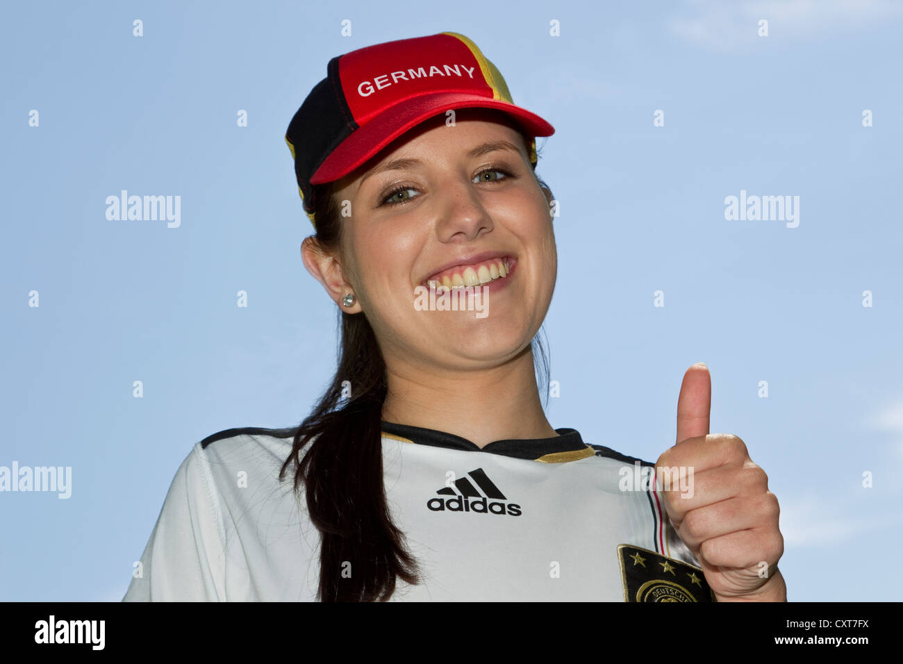 Jeune femme, fan de football portant un chapeau de l'Allemagne et de jersey, portrait, faisant un geste thumbs-up Banque D'Images